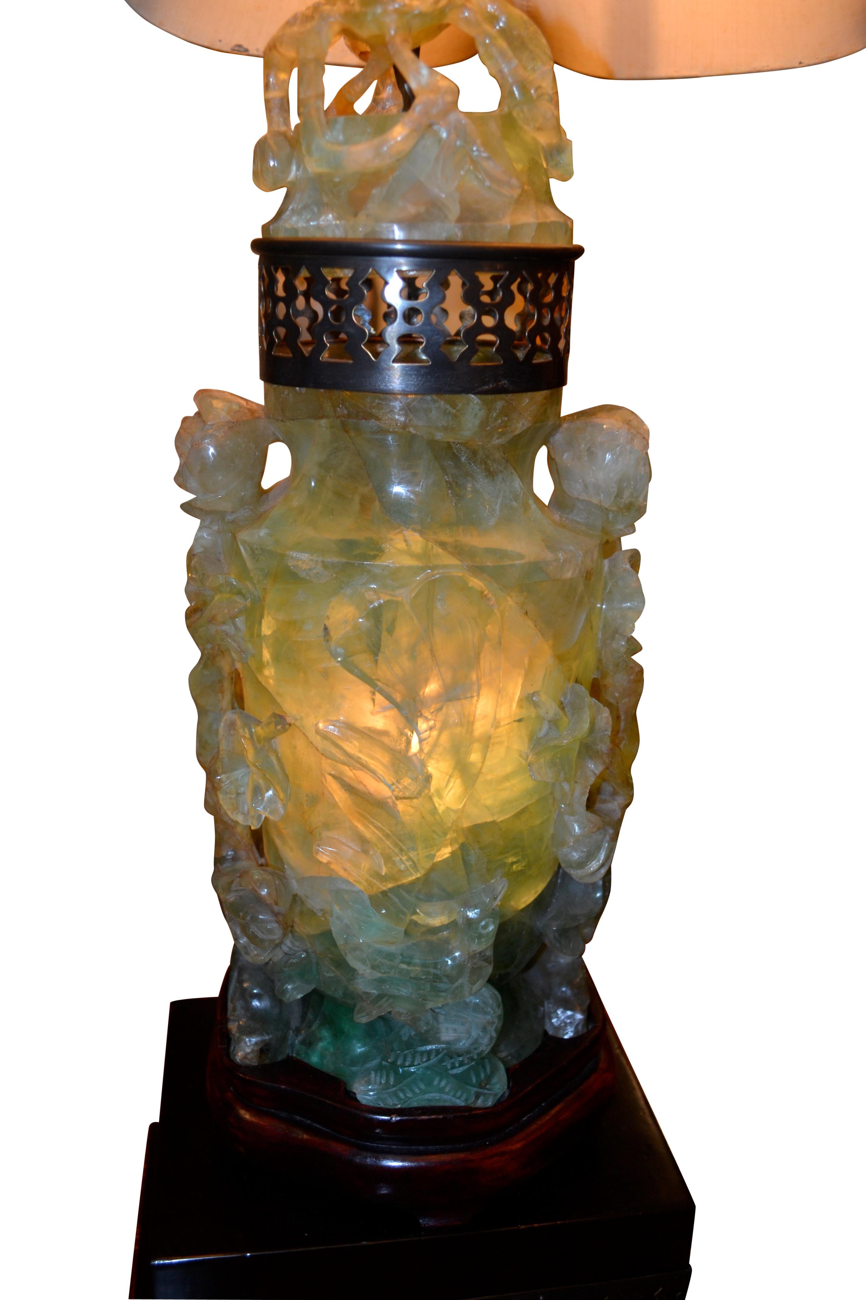 The stone bodies of this type of interior illuminated lamp are often referred to as quartz, jadeite or even jade but are in fact of the fluorite family, a softer sone more easily carved. The hollow urn bodies are carved all around with tree trunks