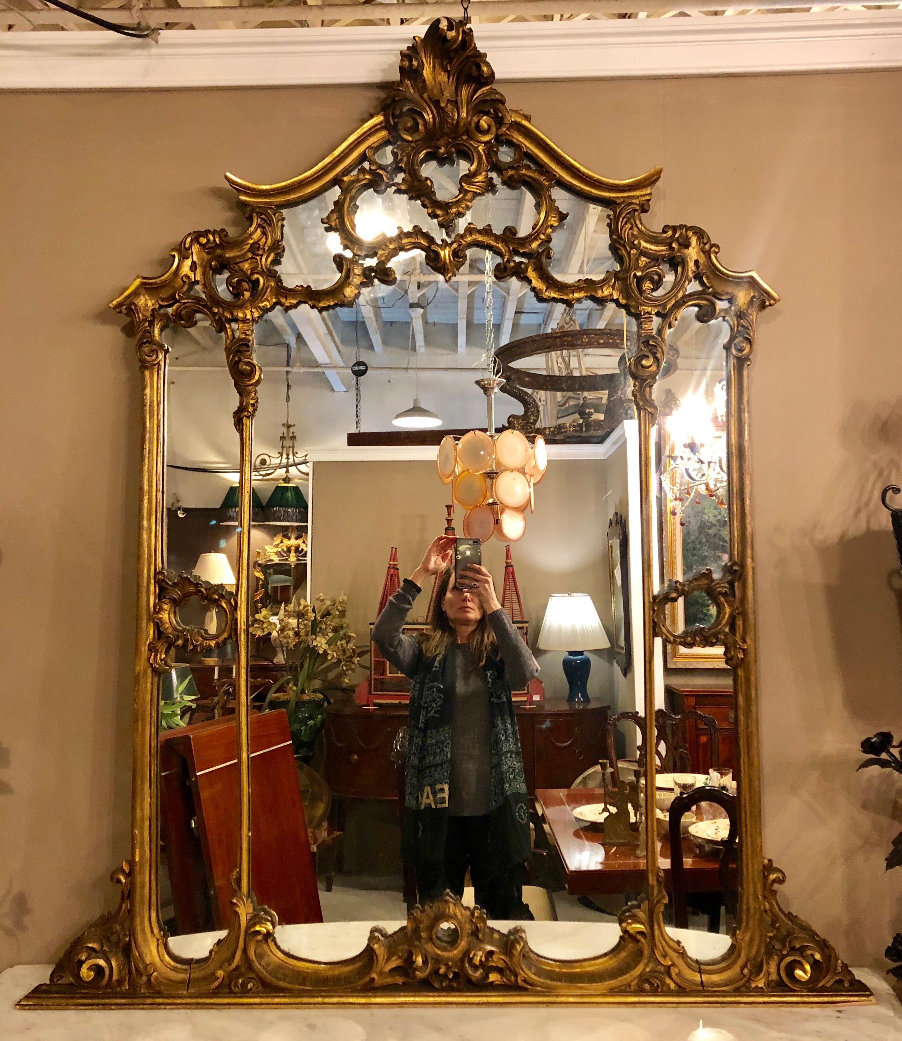 A large carved Louis XVI style French gilt gold over the mantle or wall mirror. This finely carved and impressive gilt gold wall, console or over the mantle mirror is simply stunning with its shell and scroll carvings giving the illusion of three