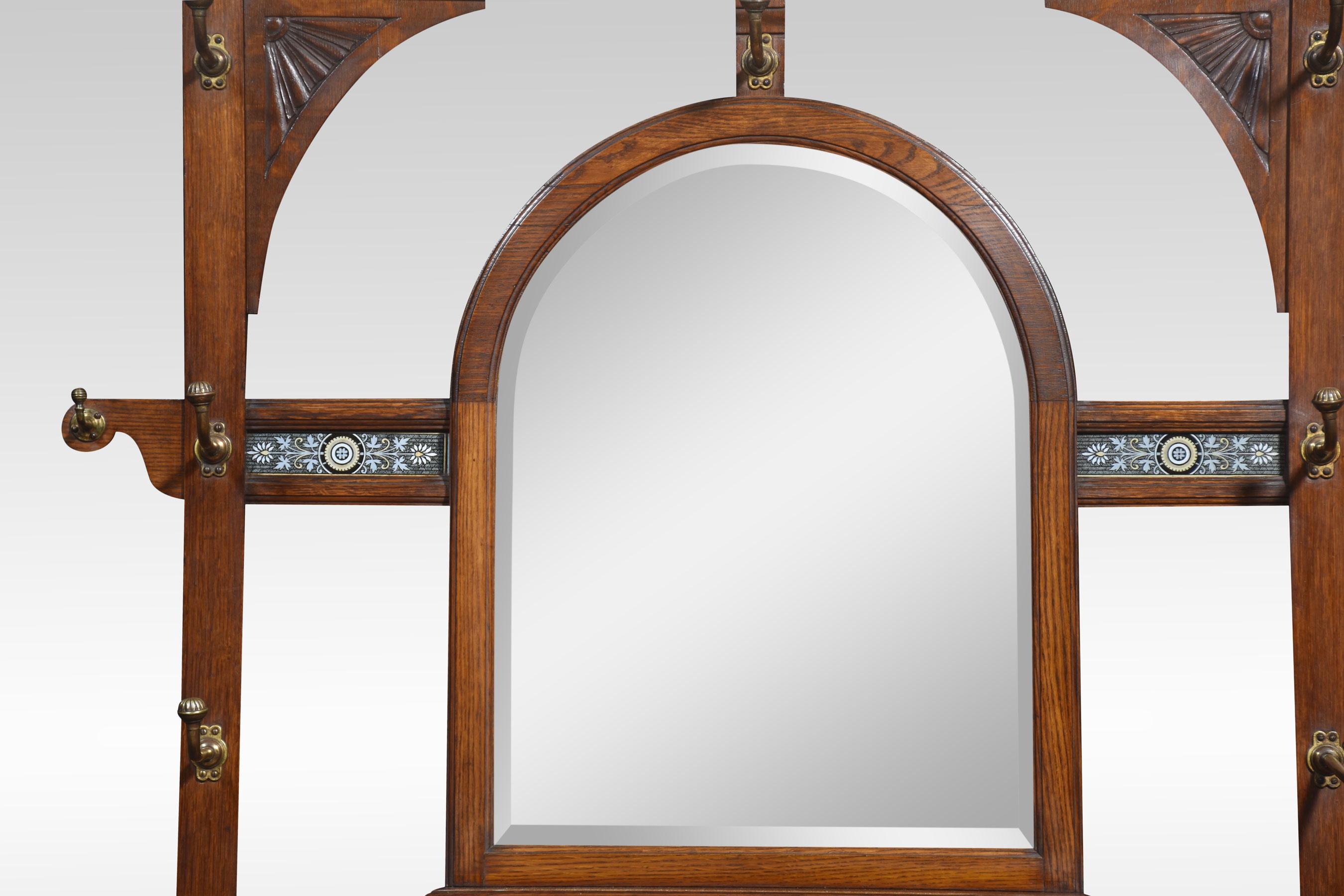 Oak hall stand, the superstructure with a central bevelled mirror surrounded by turned hooks and decorative tile plaques. The base section having a marble top above a pair of panelled doors opening to reveal a shelved interior flanked by umbrella