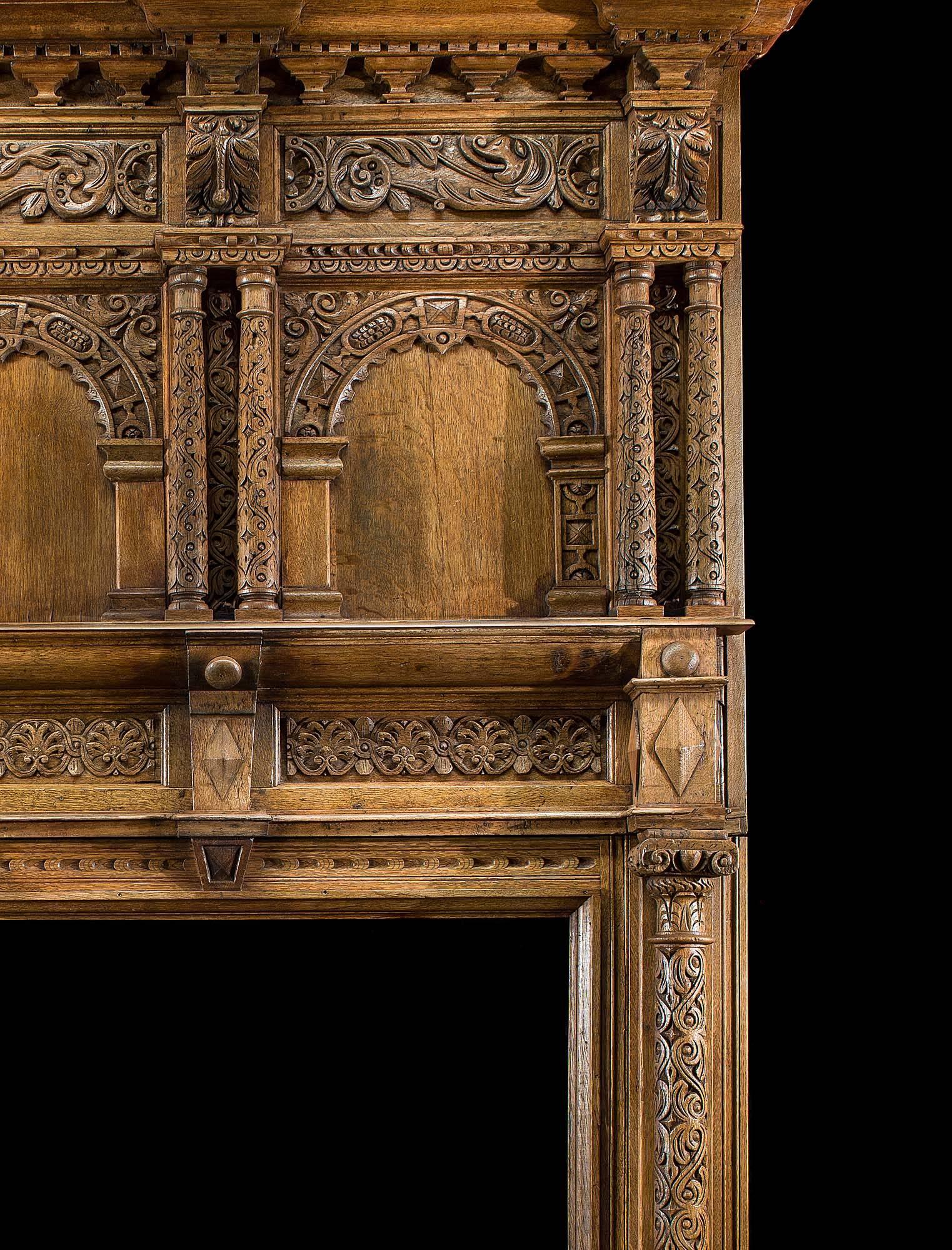 A large carved oak Jacobean fireplace surround and overmantel. The high breakfront shelf rests above bead and reel and bracket supports. The carved overmantel is embellished with a pair of scrolled foliate panels beneath which are decoratively