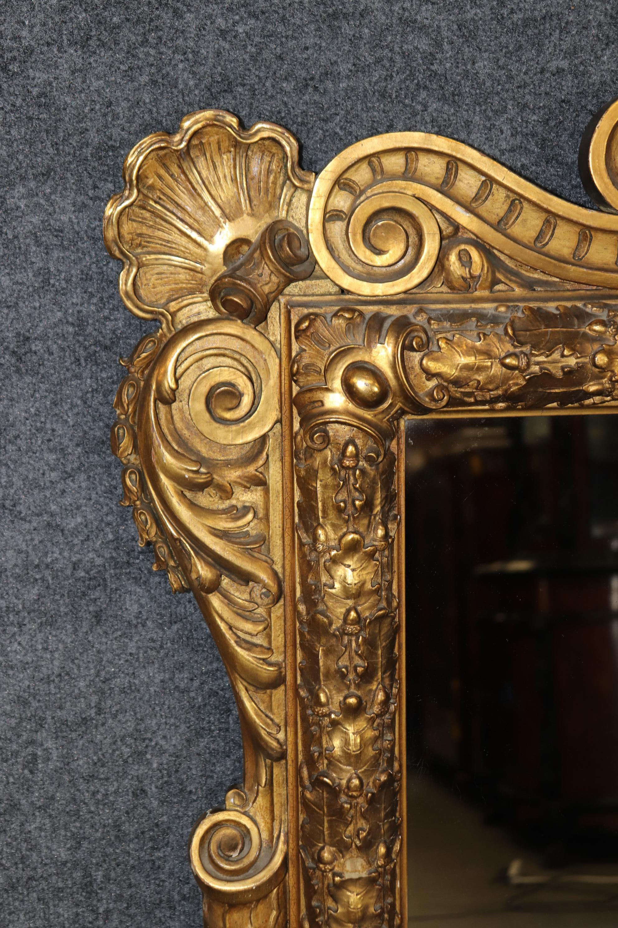 This is a superb, very very large 1880s era Regency style carved oak leaf and shell gilded mirror. The mirror retains an old time-worn distressed gilt finish with minor chips and signs of age and use. This is a very heavy mirror and has built-in
