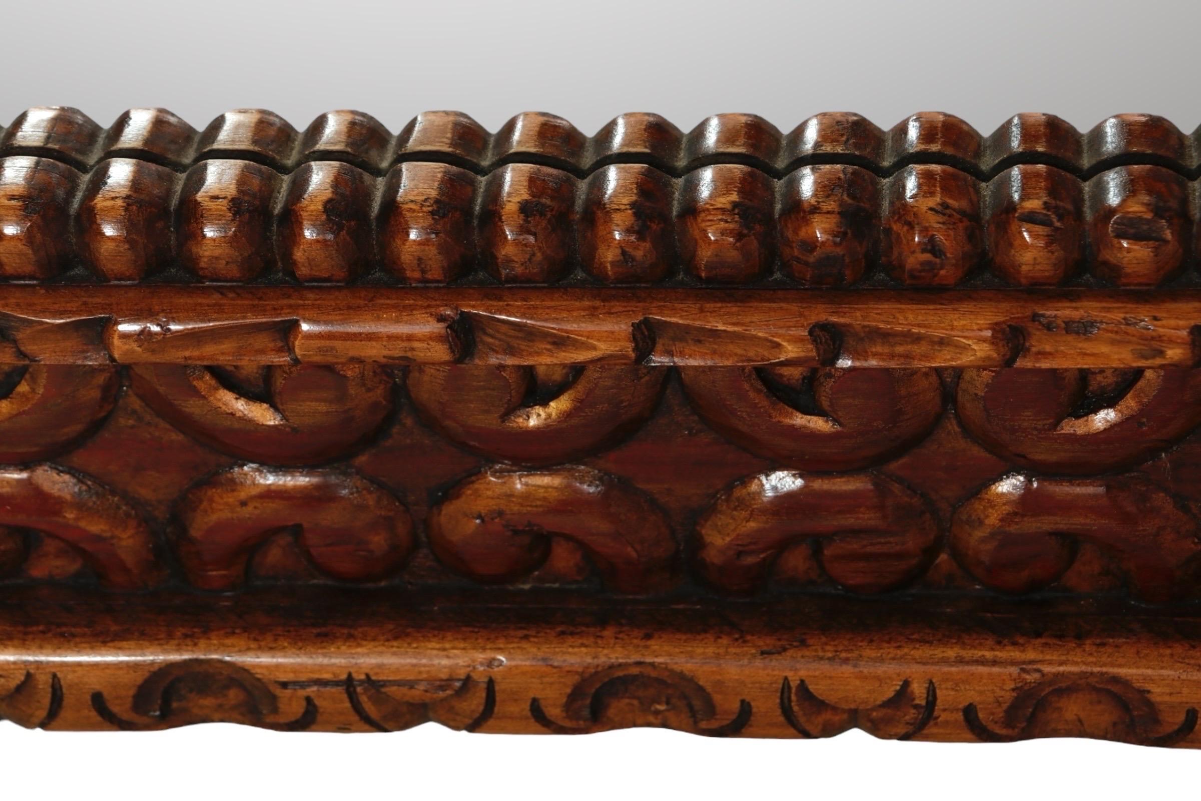 A large carved teak wall mirror. The richly carved wooden frame is decorated with c curves, scrolls and rosettes on the corners, and a beaded inner edge. The frame is finished with a gold wash.