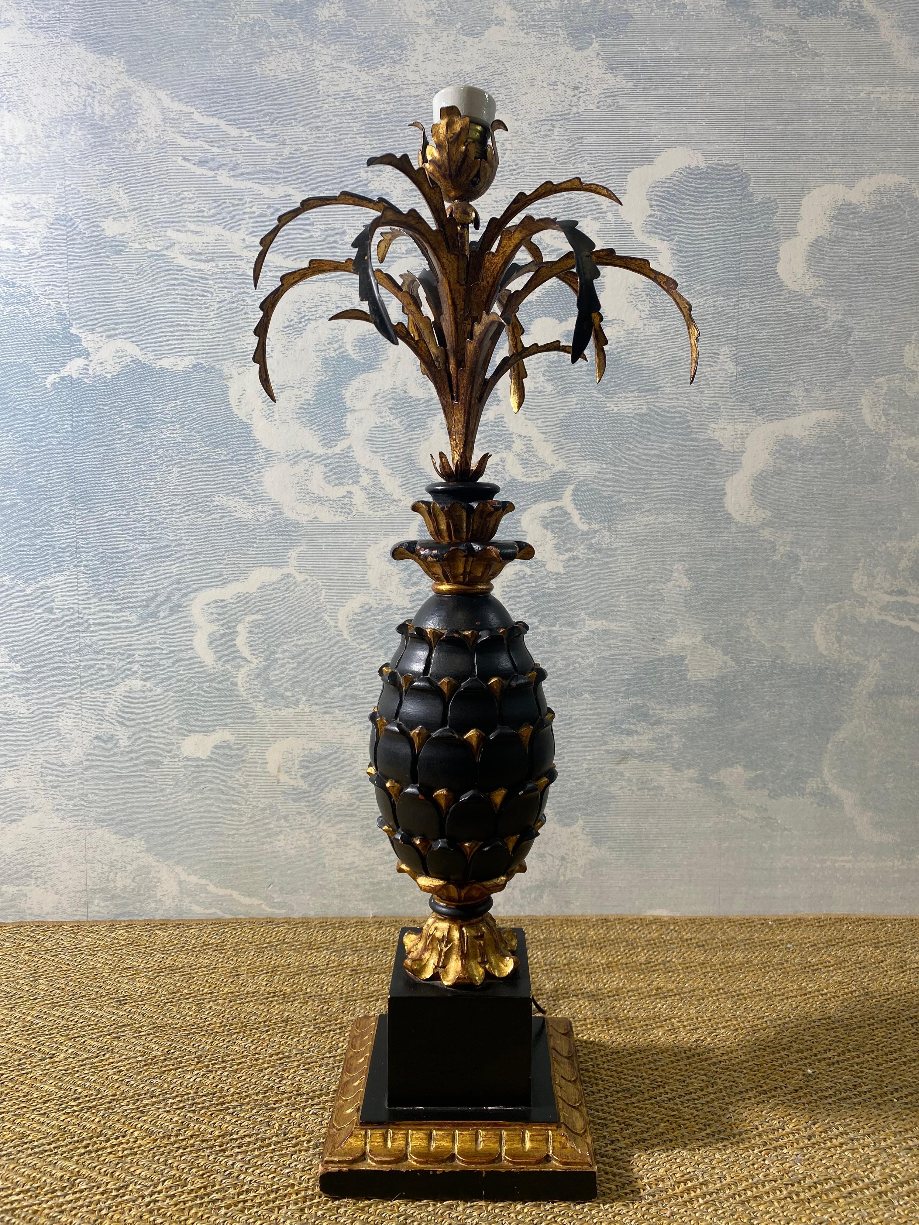 Esta glamurosa lámpara de sobremesa con cuerpo de madera tallada en forma de piña procede probablemente de la Francia de la primera mitad del siglo pasado.

Elevada sobre una base cuadrada y decorada en negro y dorado, esta luminaria bastante grande