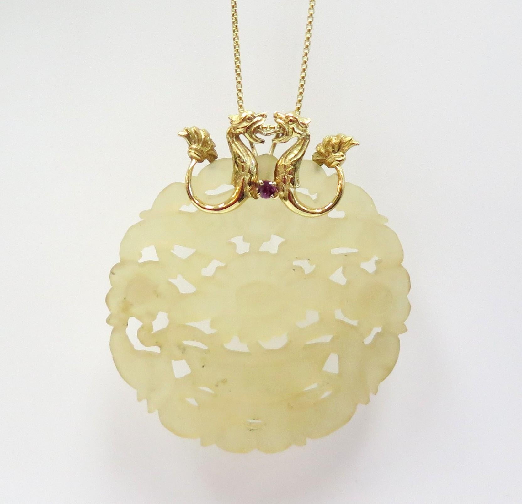 Two 14 karat yellow gold dragons that meet in the middle with a ruby and fan tails create a bail that holds a large round carved yellow jade pendant. 

Measurements: 3