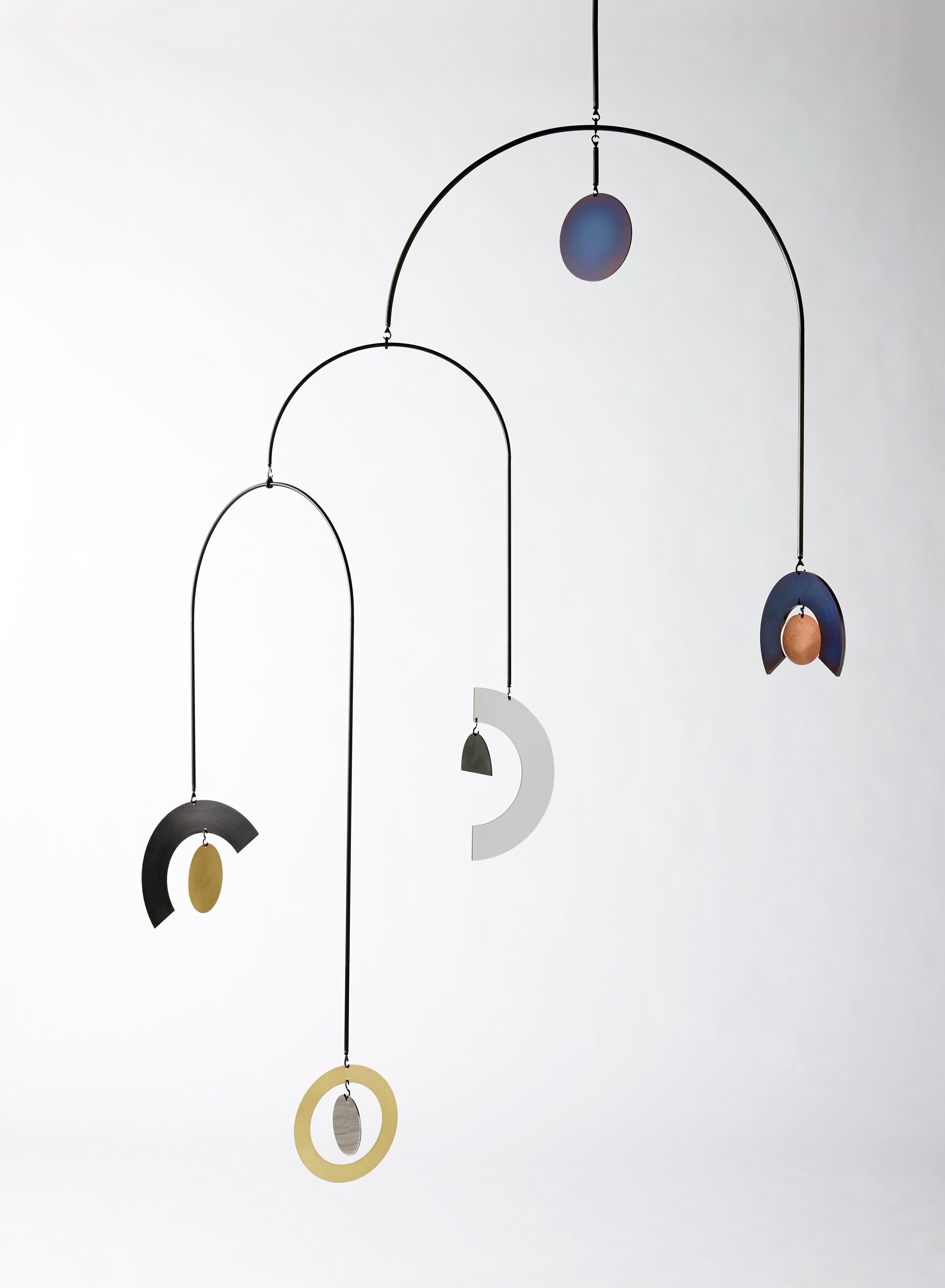 An undulating composition of discs, rings, half moons and rainbows cascade from large sweeping arcs to create a hypnotic hanging sculpture. Each object has a unique patina that draws inspiration from our solar system. Surface textures that recall