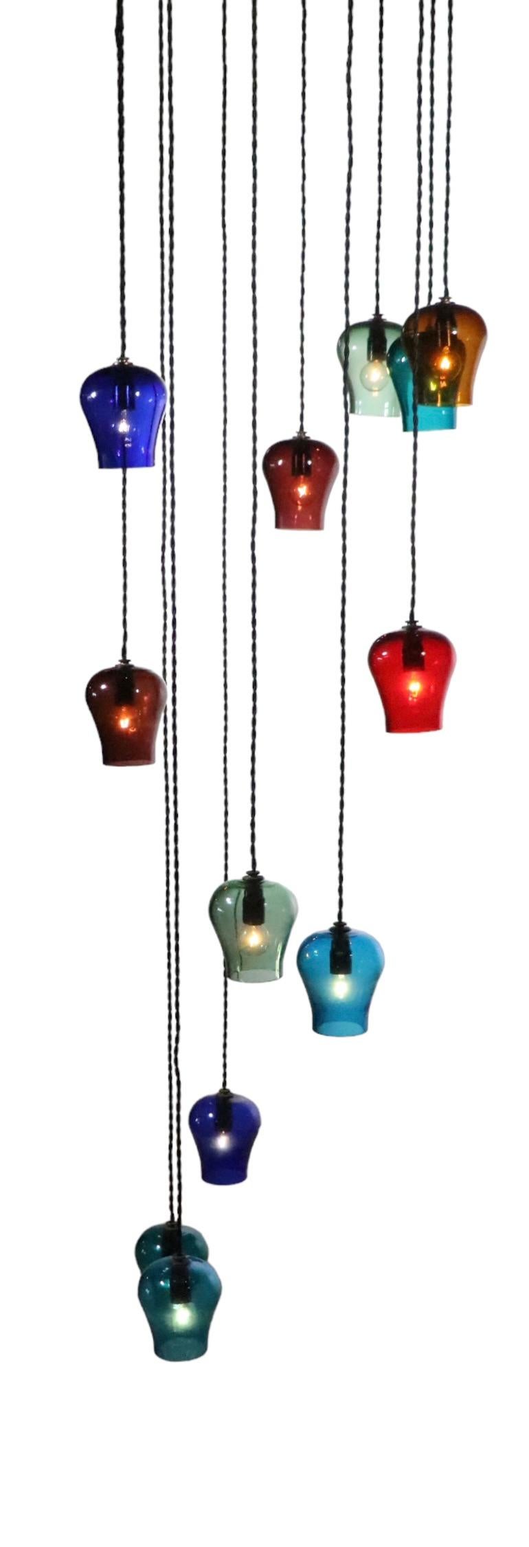 Impressive Mid Century chandelier, having hanging glass globes,  suspended from a large ceiling canopy ( 18 in. dia. ). The fixture has  12 glass  bell shaped shades, each of a different color, and each different in length of drop. The shades hang