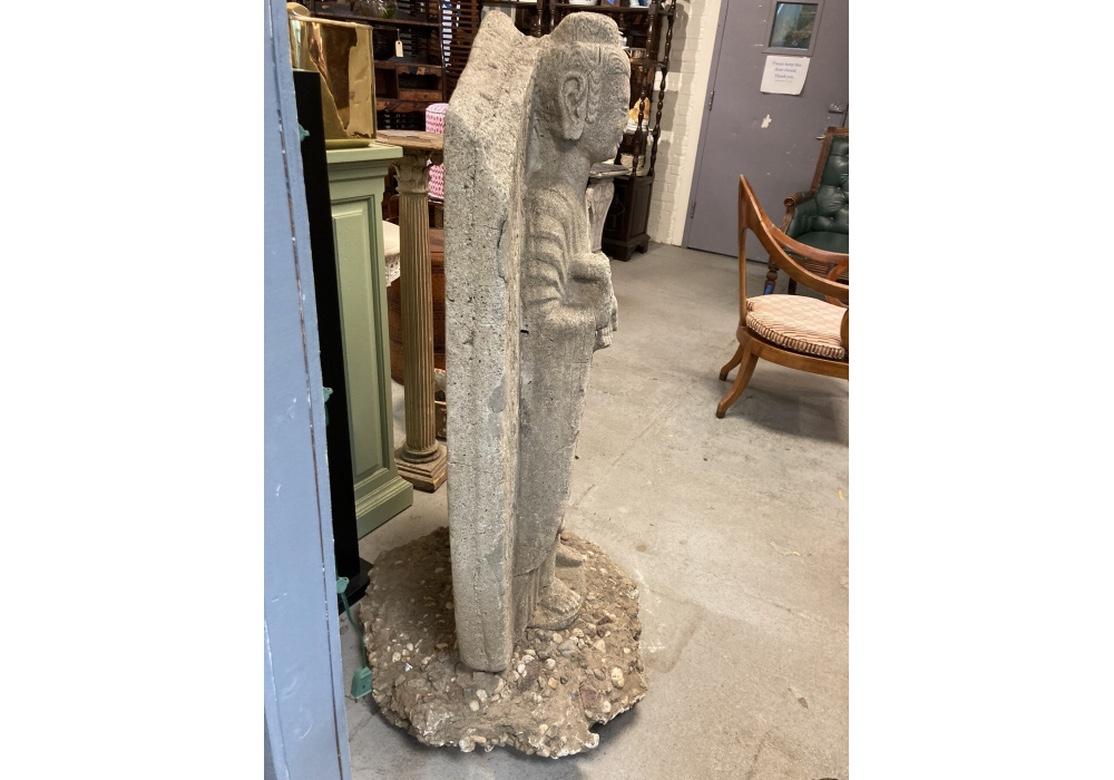 Un'imponente figura di Buddha da giardino in pietra o cemento di buone dimensioni e dal volto sereno. Le mani della figura sono nella posizione Abhaya Mudra che denota assenza di paura e protezione. Il Buddha si trova di fronte a uno sfondo