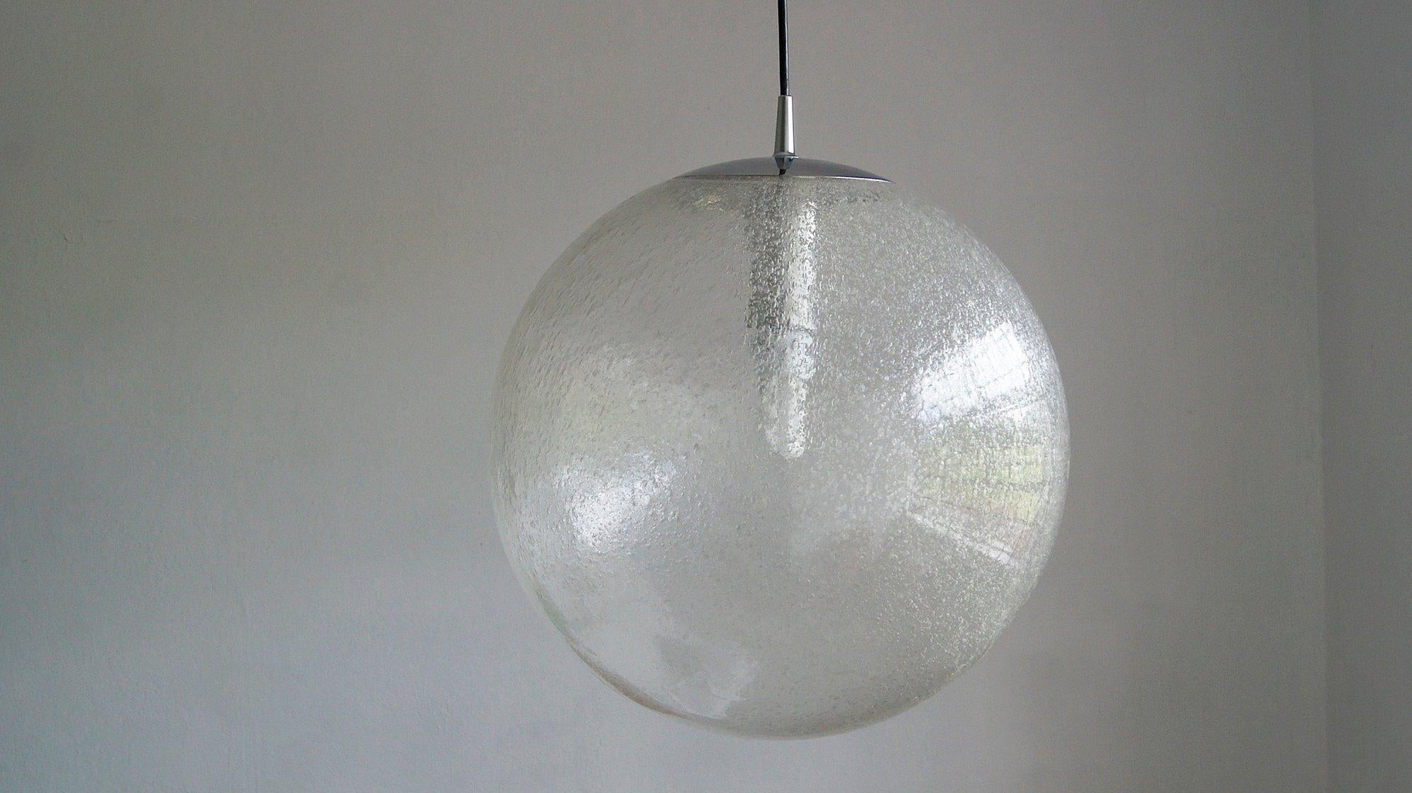 La grande lampe suspendue a été fabriquée par Peill & Putzler .
Fabriquée à partir d'une sphère en verre clair soufflé à la main, elle est complétée par une finition chromée qui lui confère un aspect original.
Comme la sphère de verre est soufflée à