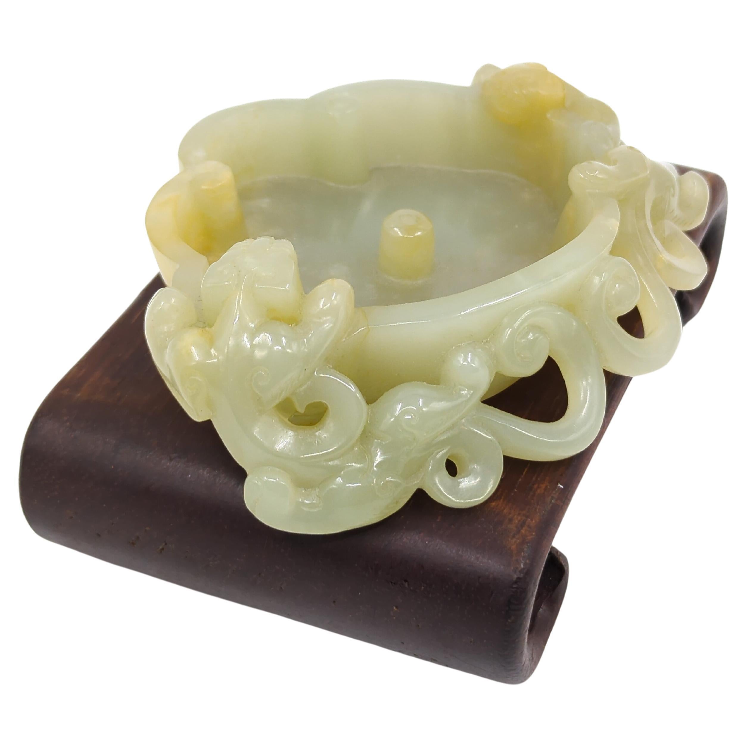 A fine antique Chinese hand carved jade brush wash, in ruyi head form, sides flanked by 2 climbing hydras, and bottom carved with three raised circles feet

Size: H: 32 mm W: 117 mm D: 93mm
Height on stand: 87.5 mm
Weight: 189 grams
circa 1850, Qing