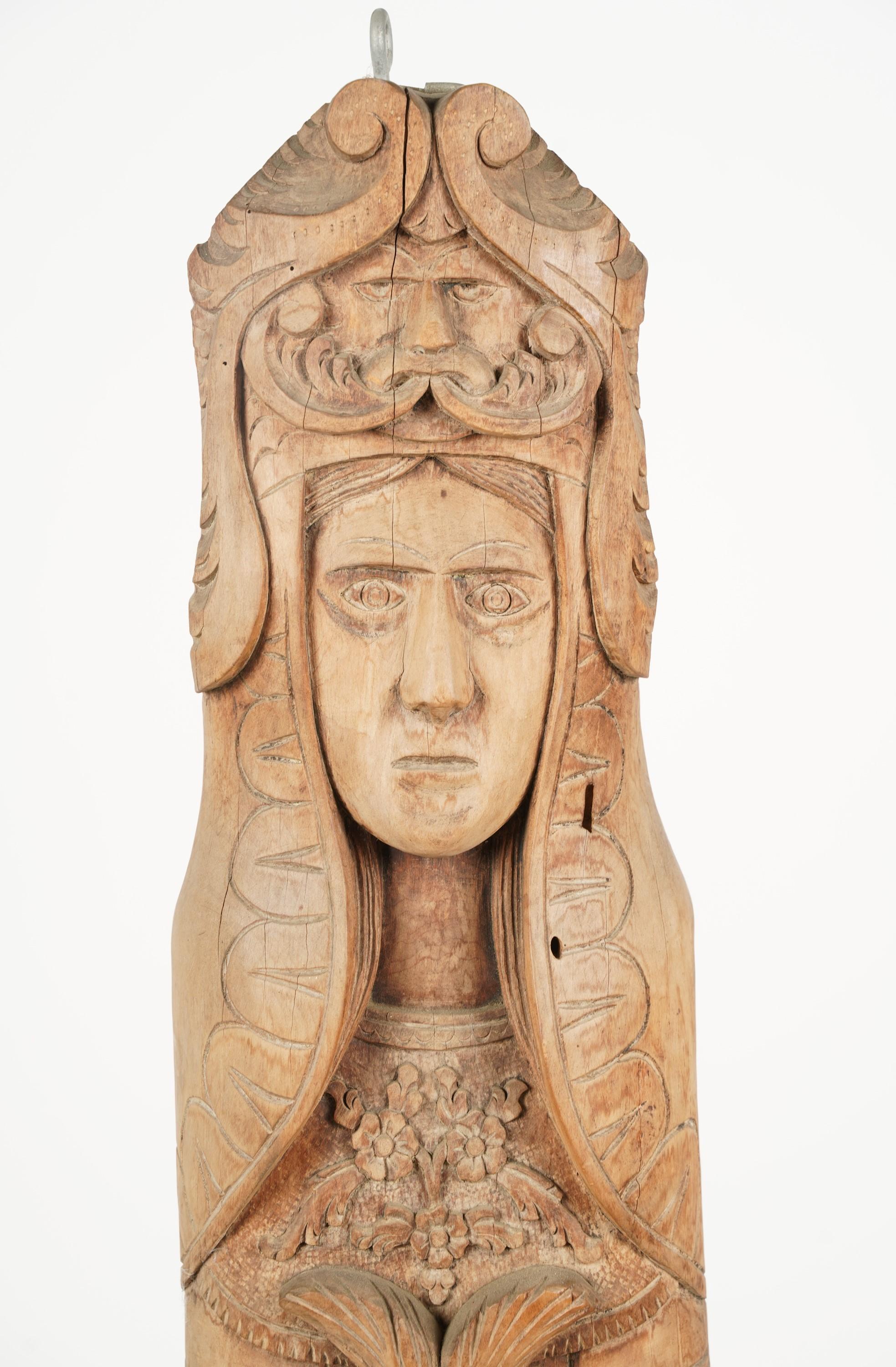A large, heavy, intricately carved, rather engaging wood folk art pagan totem figure of a woman carrying a three-headed fish with the God of Wind (North wind or perhaps an Anemoi) symbol above her head.  Her captivating yet stoic gaze and