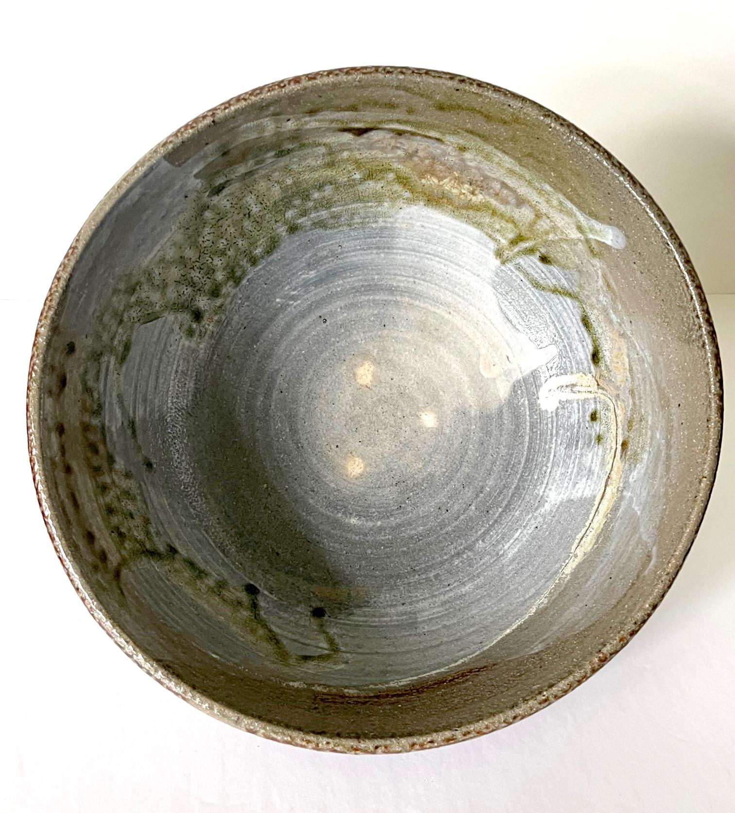 A large ceramic bowl by Japanese American artist Toshiko Takaezu (American, 1922 - 2011). The deep form bowl features a robust body of thick wall, supported by a short round foot ring. The interior surface showcases an expressive glaze pattern that