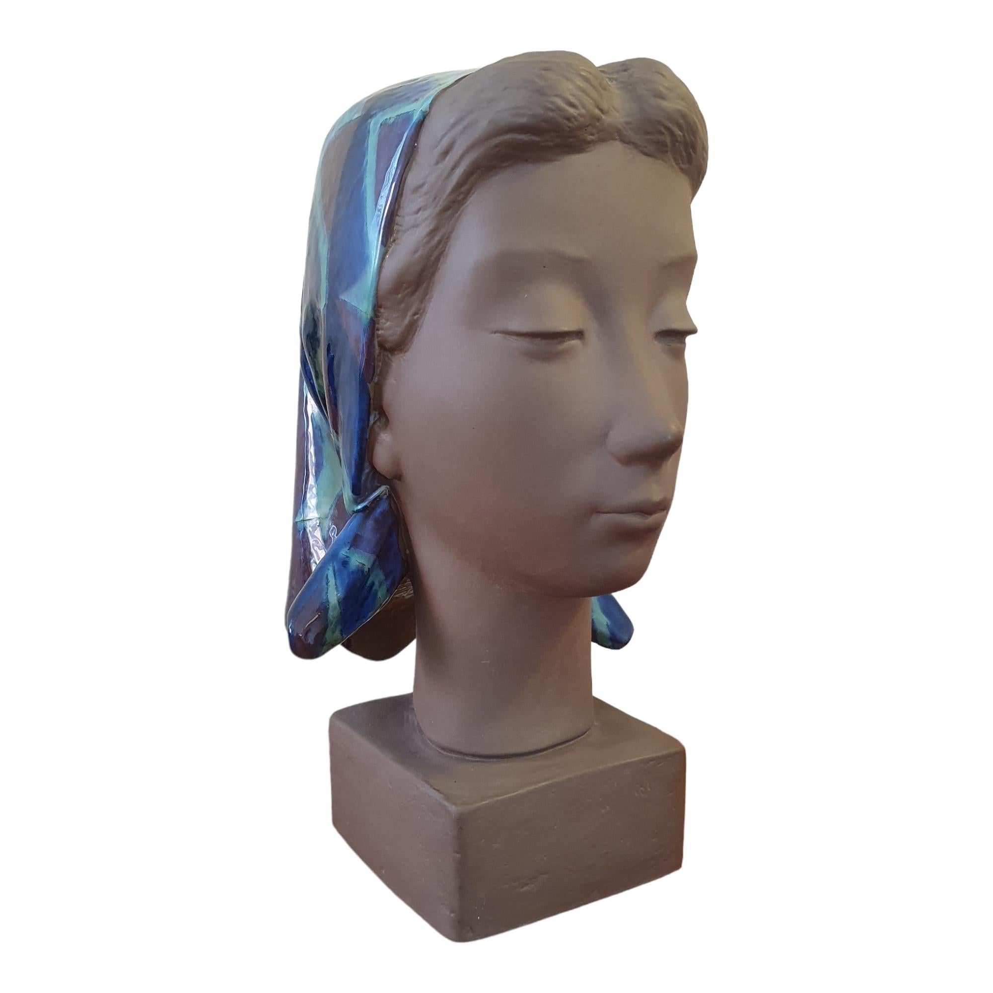 A large and beautiful bust of a woman with closed eyes and a serene look on her face. This is a classic Johannes Hedegaard sculpture with a playful balance between the matte finish of the ceramic and typical blue and greenish glaze that is almost