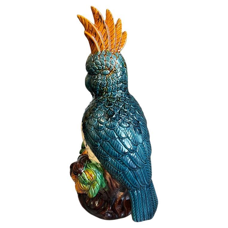 A tall bright ceramic bird sculpture in the style of Meissen. Glazed in blue, green, orange and brown polychrome, this large bird sculpture will be a wonderful accent to a bookshelf or credenza. He has a tall feathered plume of feathers which is