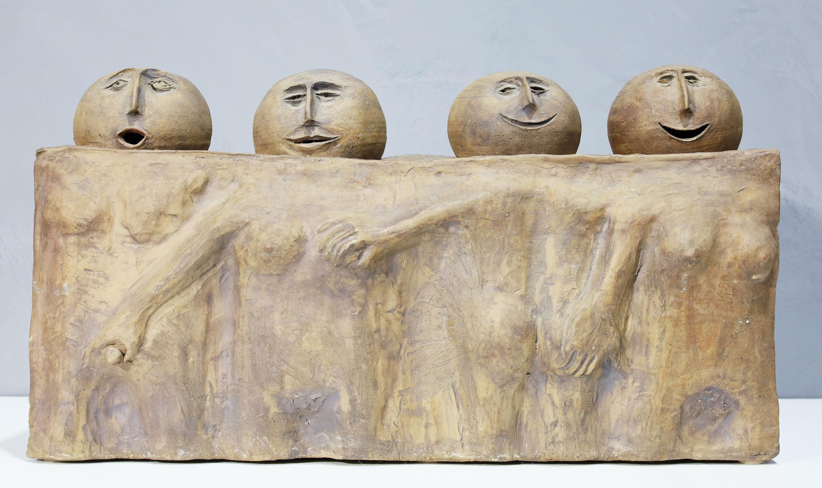 Somewhat cartoonish a large scale ceramic sculpture of four heads resting on a single block form ceramic base. Figures molded and incised in base. Base is hollow and has a beautiful blue glaze feature on the backside.