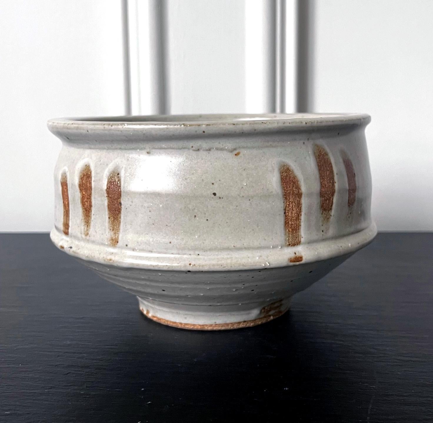 A stoneware center bowl by American ceramist Warren Mackenzie (1924-2018). Thickly potted in rather distinct shape with a prominent mouth rim and tapered lower body, the bowl appears both robust and elegant at the same time. The surface was covered