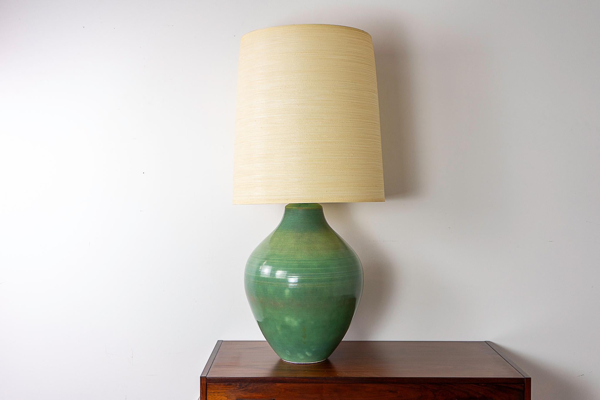 Ceramic table lamp by Lotte & Gunnar Bostlund, circa 1960's. Rare, striking hand thrown ceramic base with a dramatic profile and beautiful celadon glaze! Let the warm glow of their famous lampshades entice you. Excess cord slack can be neatly tucked