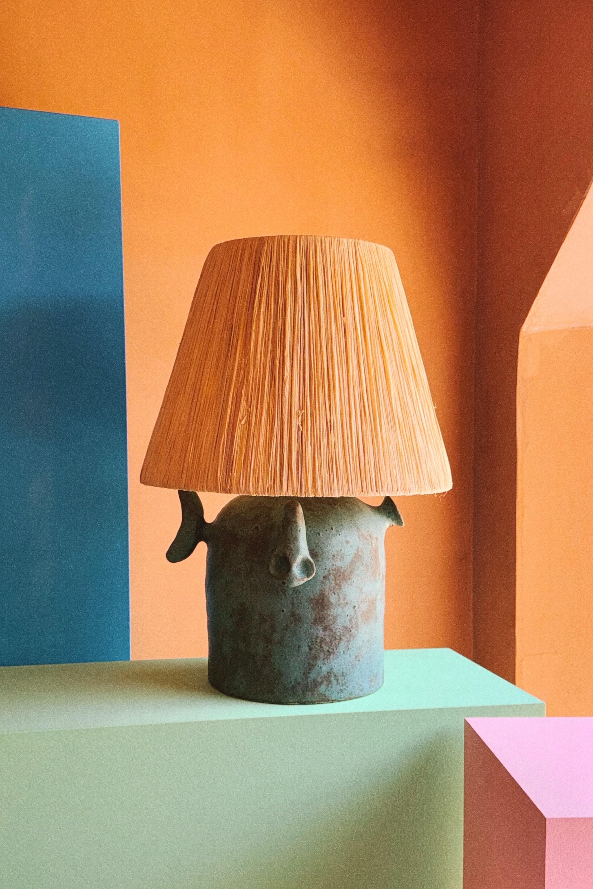 Construite à la main, cette lampe en céramique est fabriquée en terre cuite et émaillée par l'artiste, ce qui donne au corps de la lampe une patine de bronze. L'abat-jour en raphia a été réalisé à la main par l'artiste.

Tous les éléments sont la