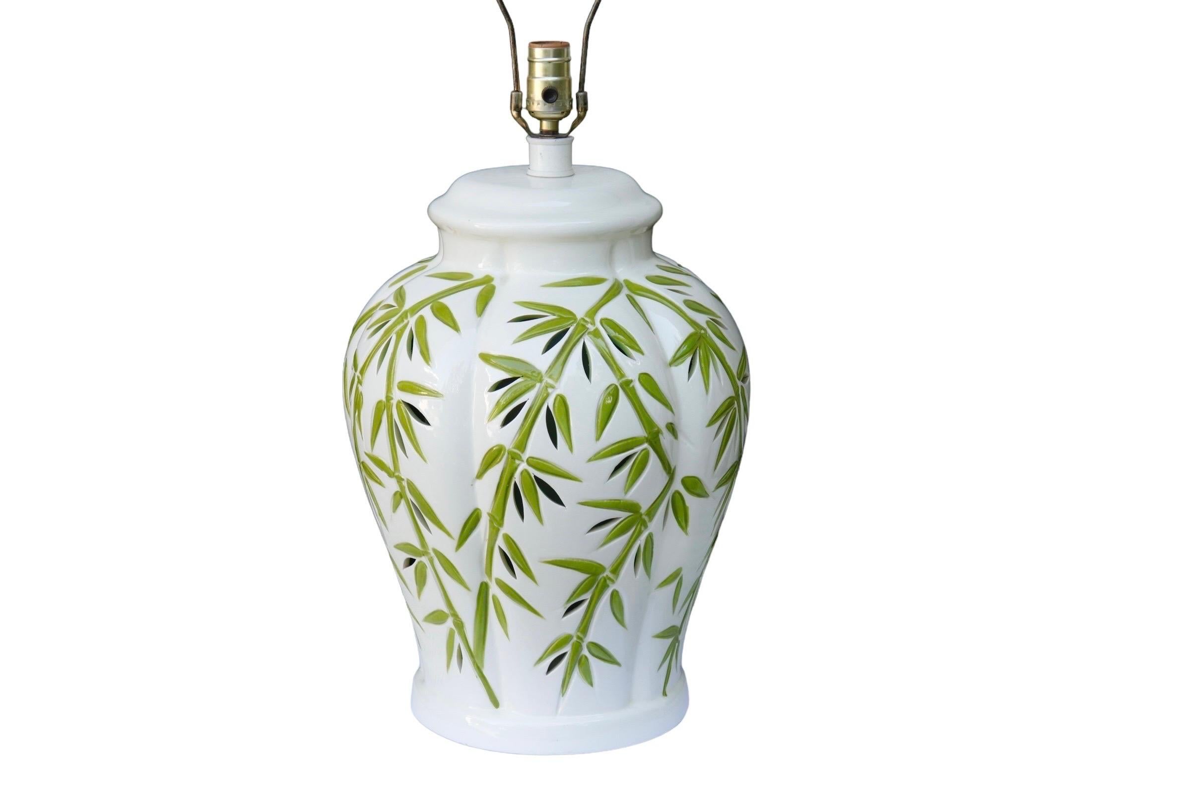 A large white and green ceramic table lamp made by Sunset Cosco Lamps. The vase is decorated with engraved and painted stylized bamboo, pierced with foliate shapes. At the base is a radial switch that turns on an interior light, and there is a