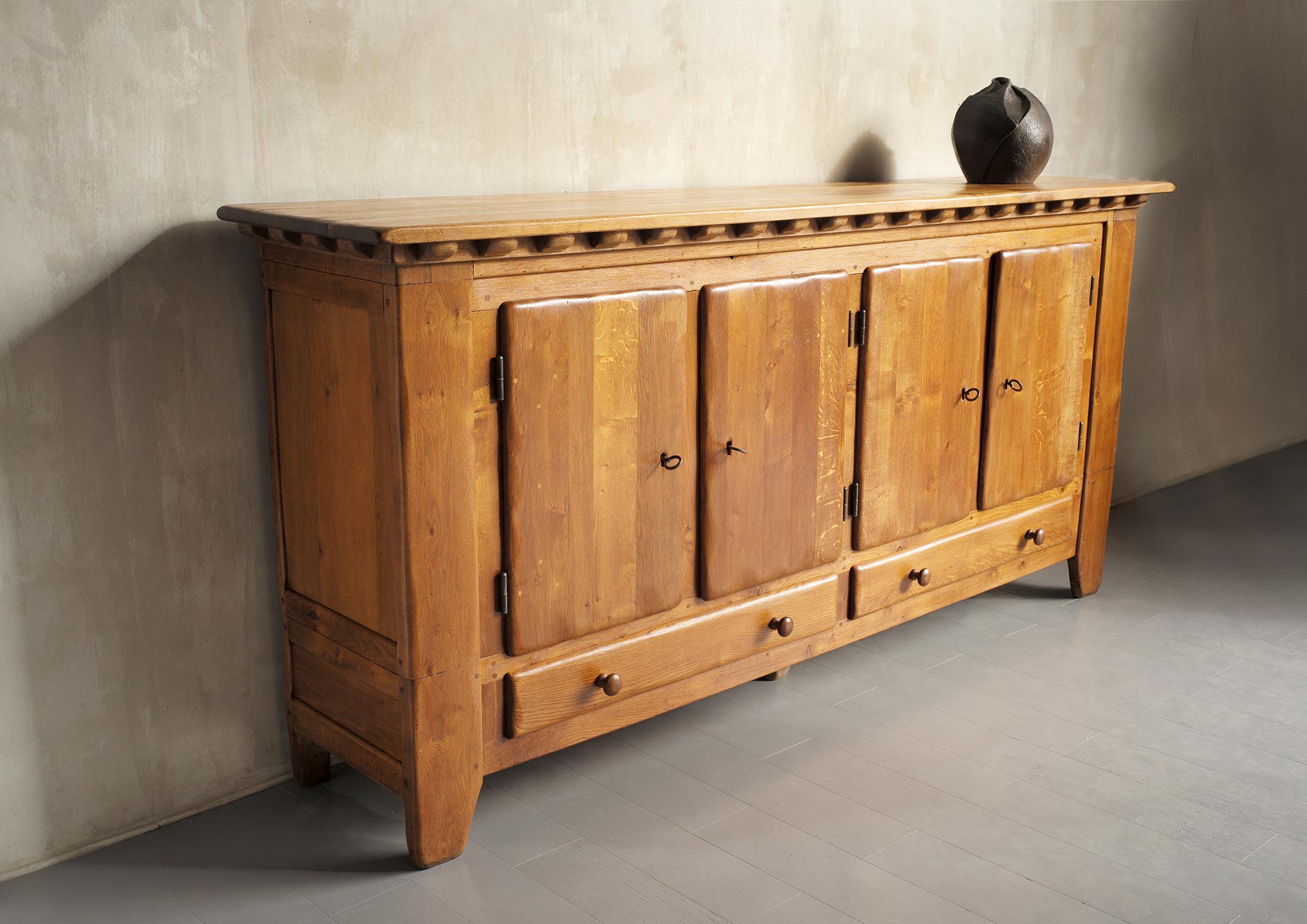 Important sideboard in solid oak, France 1950. Everything in this creation is oversized, the doors are worked in thickness and on the surface, the keys and the spring bolt system are forged, the top is decorated with wooden inserts and a series of