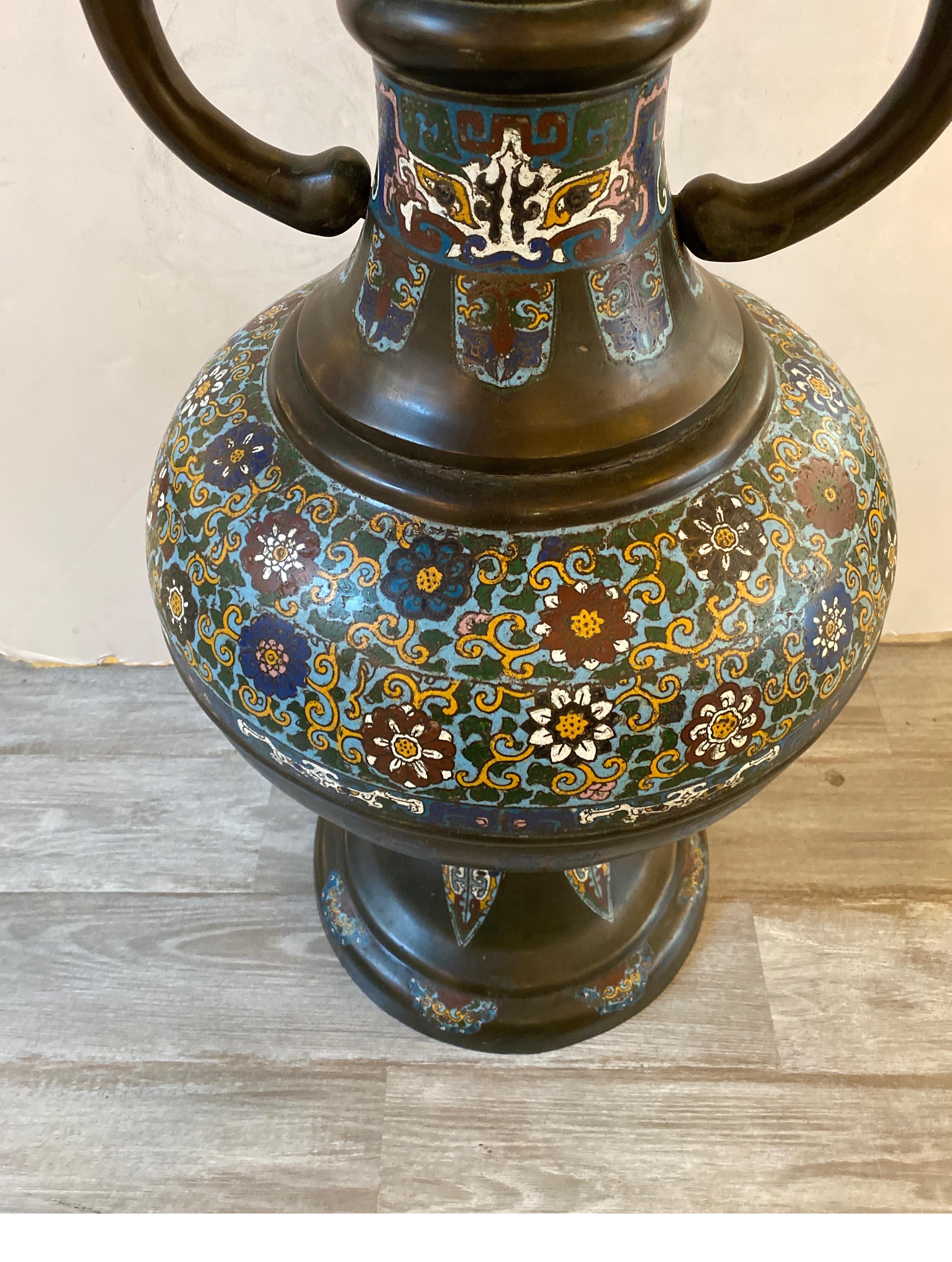 A large cast bronze and champlevé enamel palace vase. The patinated bronze with inlaid enamel decoration with mythical cast bronze dragon form handles.
