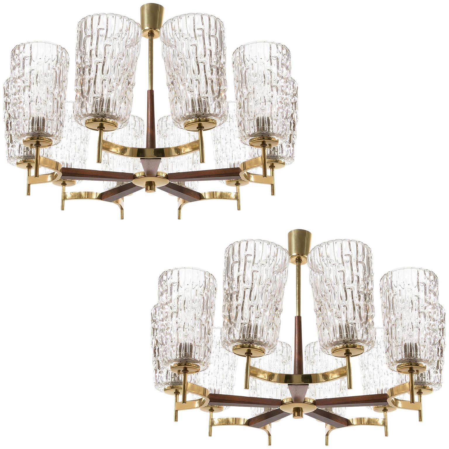 A pair of impressive ten-arm chandeliers by Rupert Nikoll, Vienna, manufacured in Mid-Century, circa 1960 (late 1950s or early 1960s). 
The fixture is made of a nice mixture of materials: large textured clear glass lamp shades, brass and warm walnut