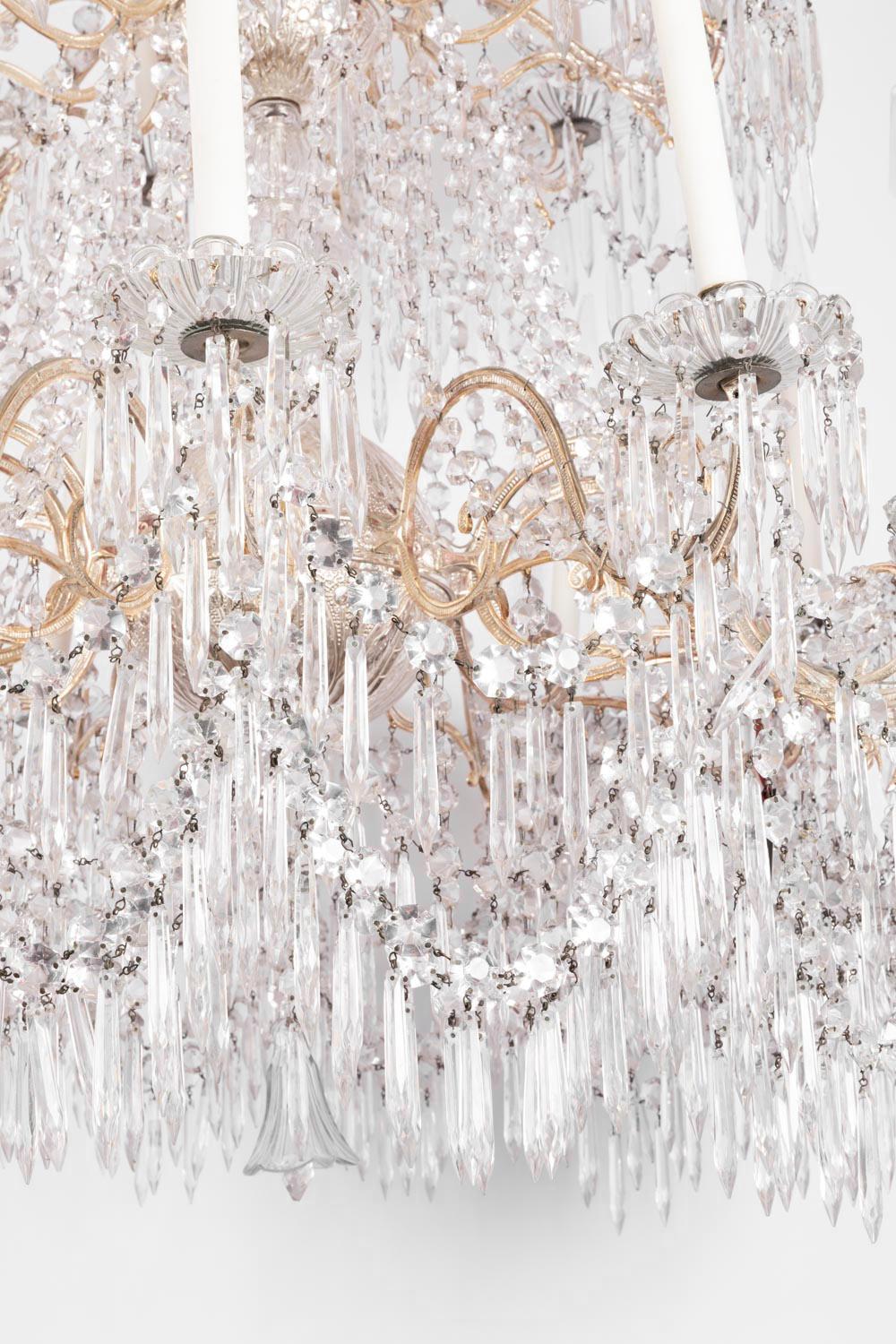 Large chandelier with a silvered bronze structure composed of 24 fires on two ranks.
Model with a 6 branches bronze crowning in foliage scrolls shape decorated by crystal tassels swags in form of ice cubes and facets octogons. 
Central shaft