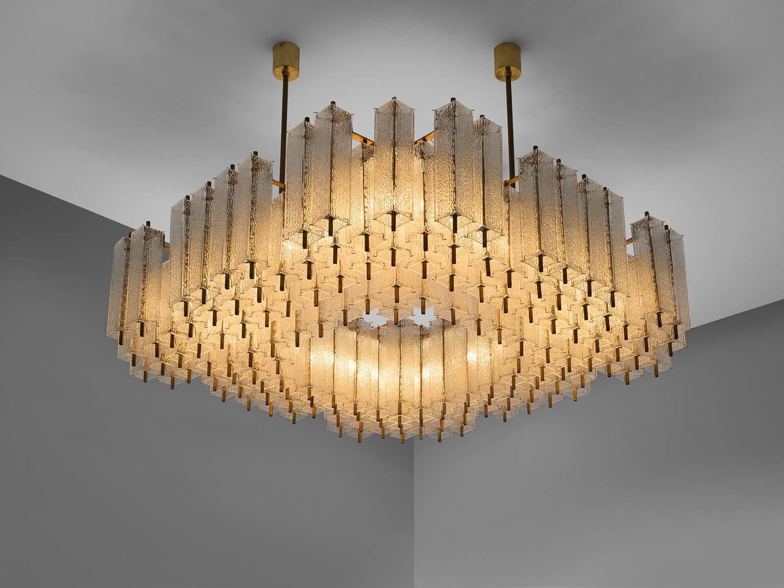 Chandelier, in glass and brass, Europe, 1970s. 

Large square chandelier with a great amount of rectangular structured glass shades. The frame is made of brass and holds numerous structured glass 'tubes' with a brass centre. Due the combination of