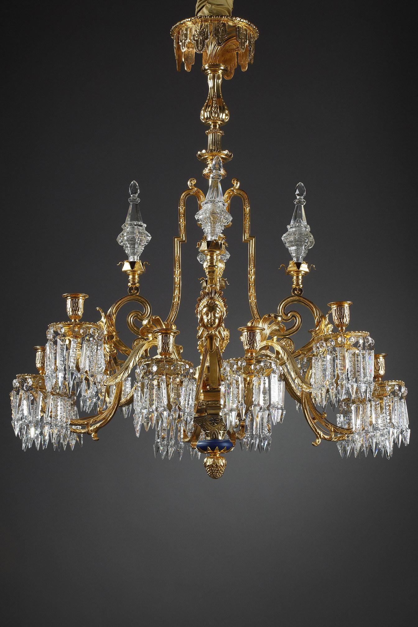 A large ormolu chandelier with twelve lights. The central fluted shaft is decorated with seeds, water leaves and a frieze of posts. It holds sinuous branches topped by crystal daggers. The gilt bronze frame is decorated with acanthus leaves, rosette