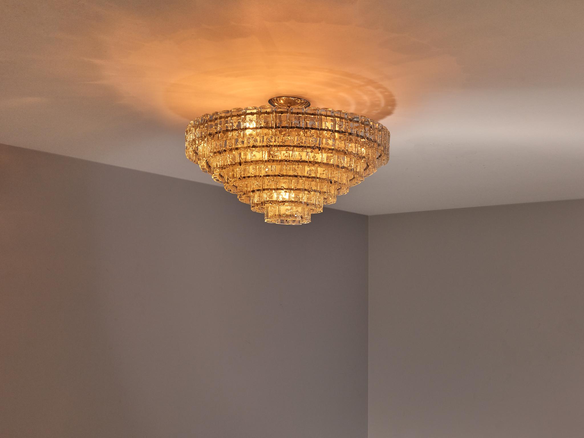 Chandelier, glass, metal, Europe, 1970s

This chandelier features a striking multi-tiered design, composed of concentric circular layers that gradually taper inward. Each layer is adorned with clear, textured glass pieces, which are elegantly