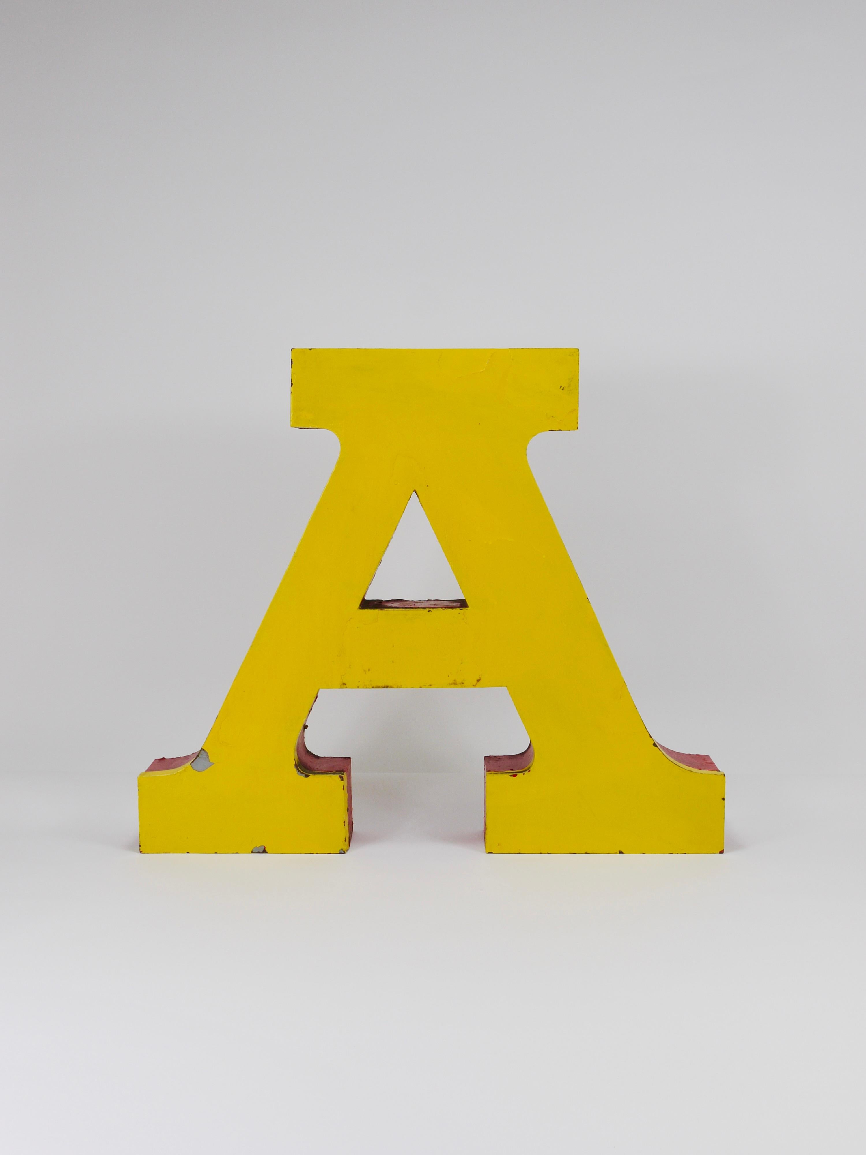 A beautiful and decorative large vintage tin channel letter “A” made of sheet metal, painted in a vibrant yellow with red sides. It is dated around the 1960s, though it may be older. The previous owner told us that the letter came from circus