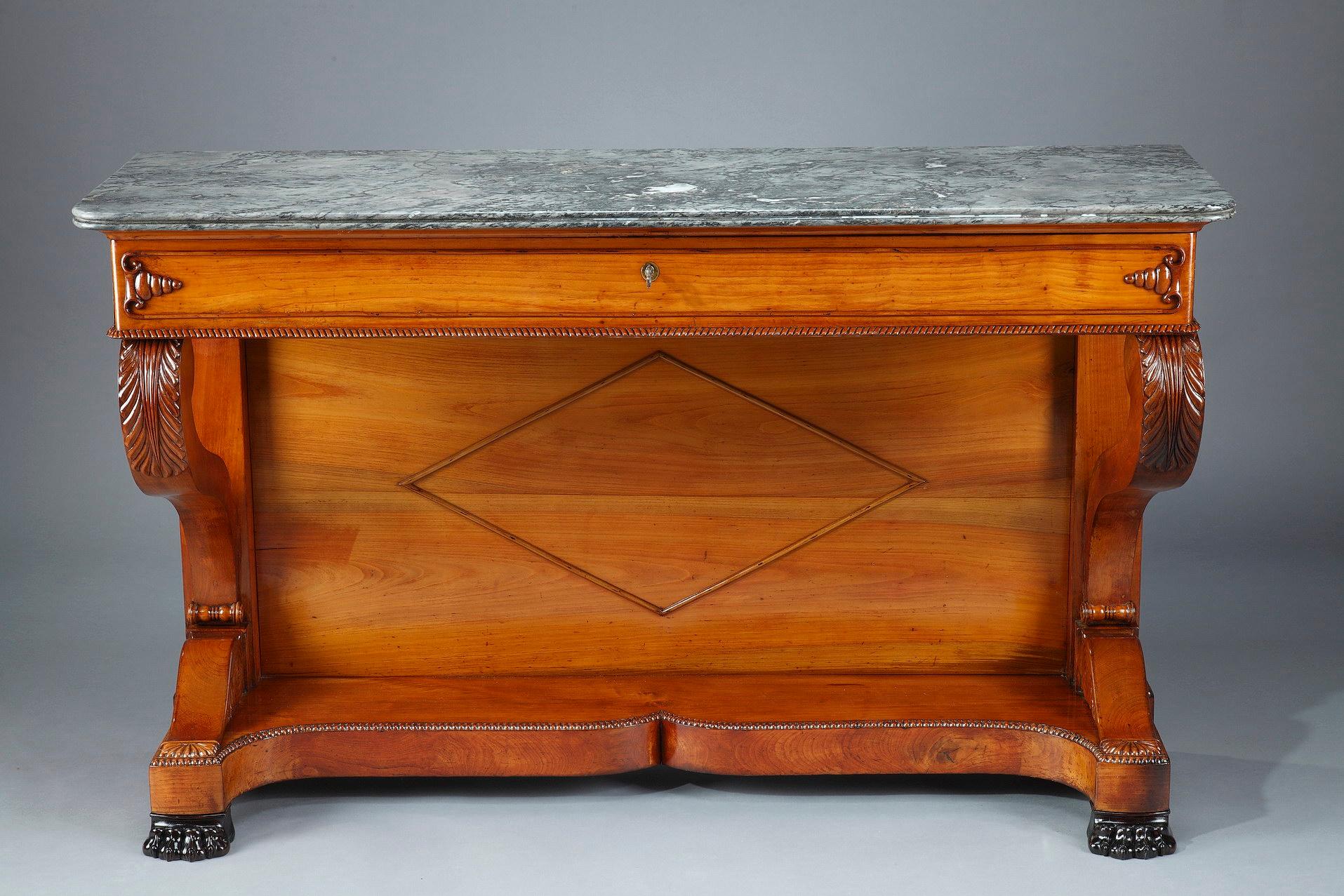 Large console in cherry wood from the Restoration period opening with a large drawer in the belt closed by a lock. The uprights are carved with water leaves and finished with claw feet joined by a moving strut with a pearl border. Grey marble top