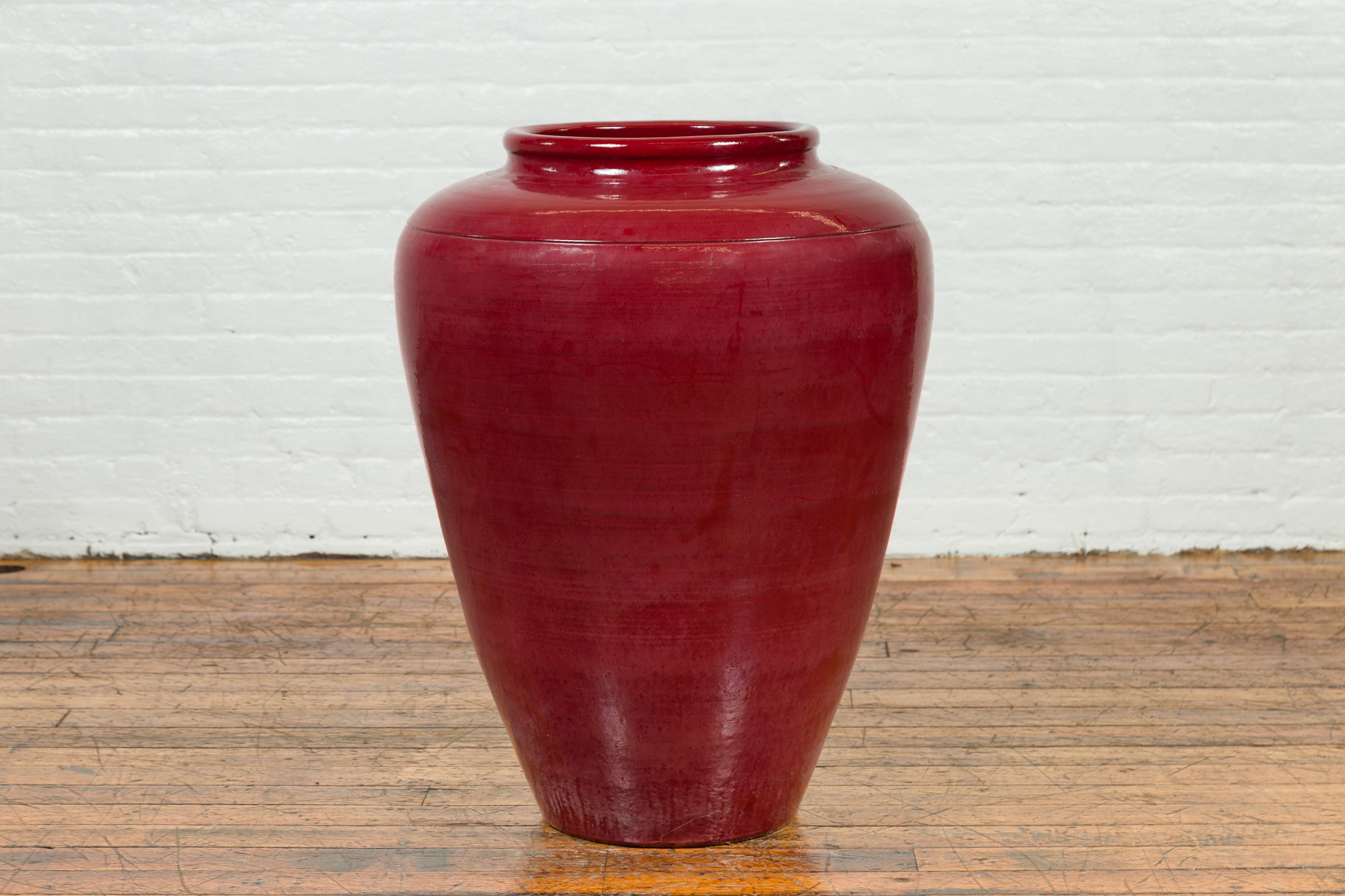 A large contemporary Thai oxblood water jar from Chiang Mai. Created in Chiang Mai, Northern Thailand, this water jar attracts our attention with its oxblood finish and large proportions. A thin lip sits above a generous body with tapering lines in
