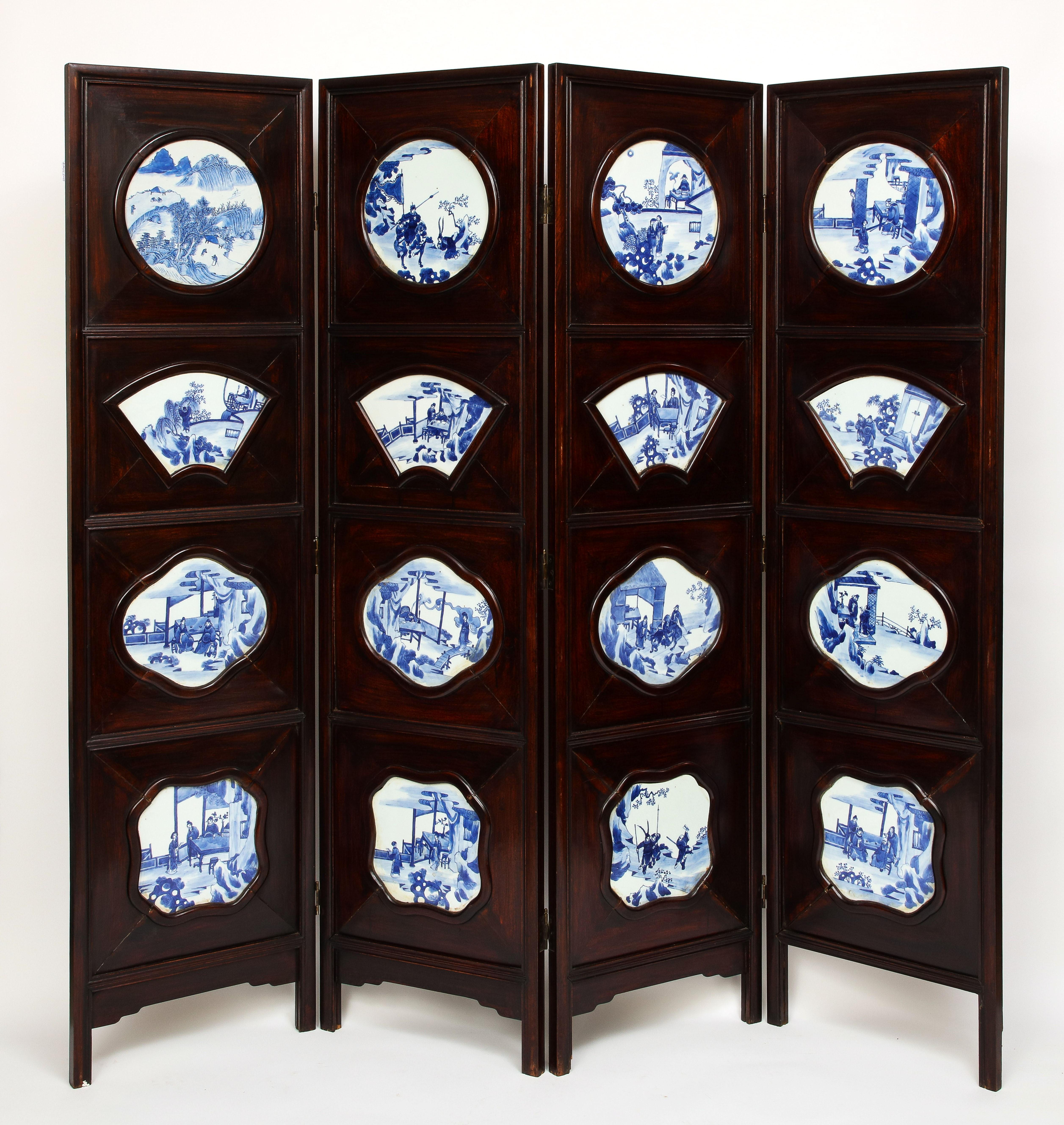 A large Chinese four-fold hardwood screen inset with blue and white porcelain plaques. The hand carved wood frame is a very dense and naturally rich and dark hardwood from China with four vertical panels and four horizontal rows of blue and white