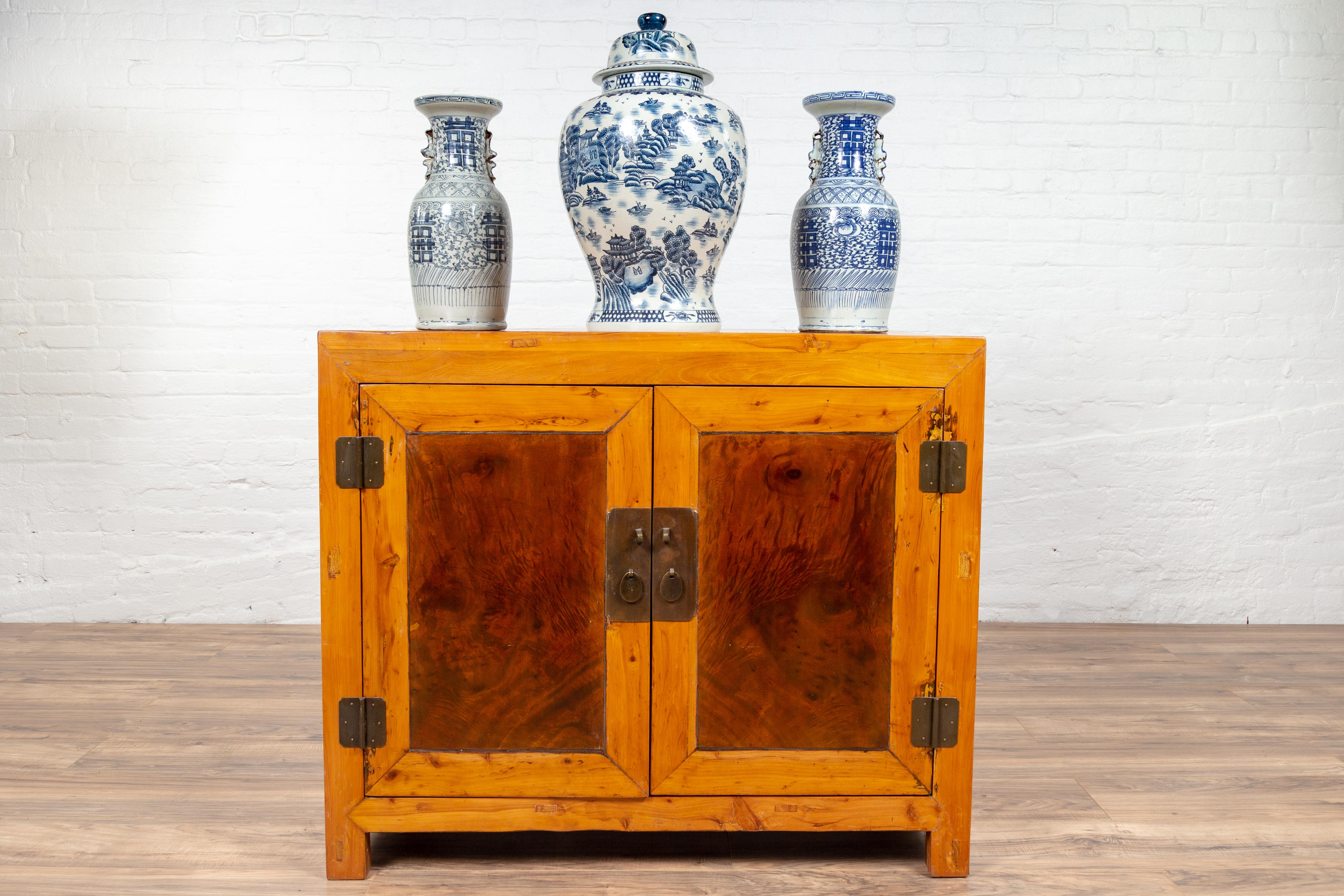 A large antique two-toned elm and burl wood Chinese cabinet from the early 20th century, with double doors and square lock. Born in China during the early years of the 20th century, this elegant cabinet presents a linear Silhouette. The rectangular