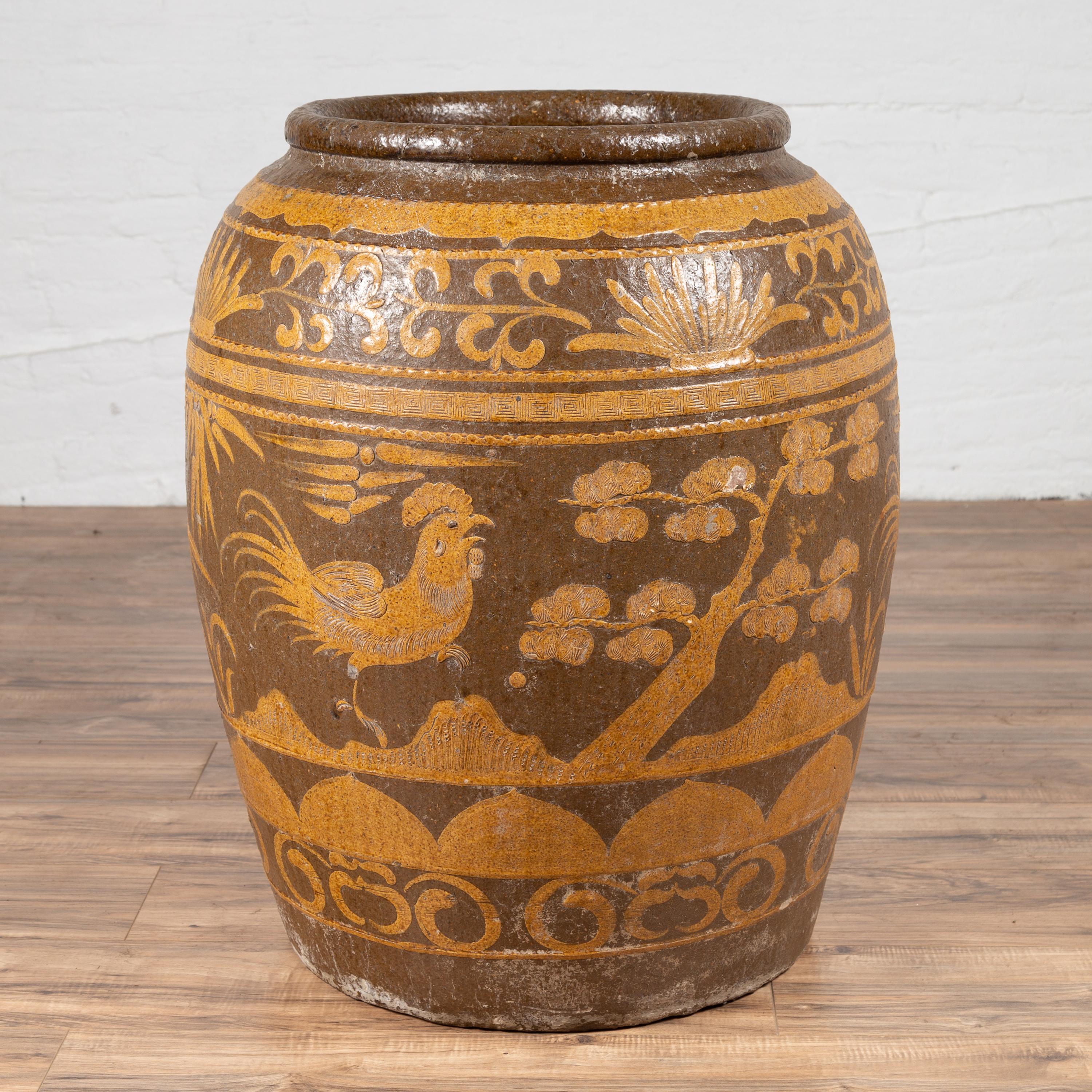 A large Chinese antique jar from the turn of the century, with mustard glaze and floral and bird motifs. Born in China in the early years of the 20th century, this charming jar features a barrel shaped body, adorned with a mustard glaze featuring