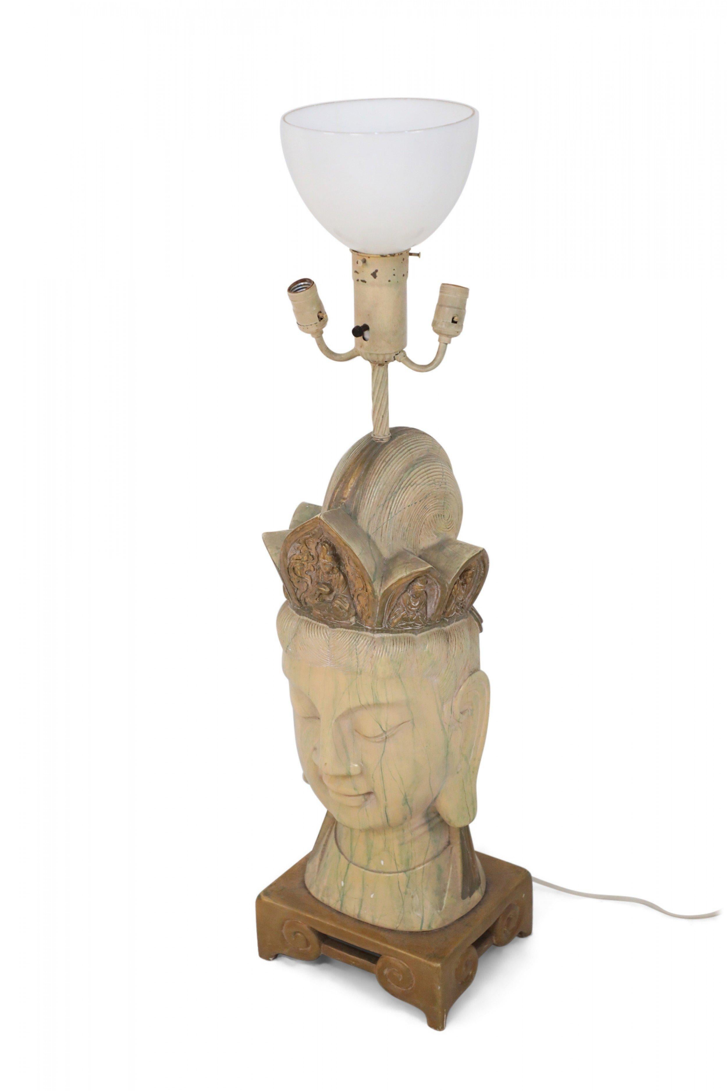 Lampe de table chinoise en bois blanchi sculpté avec tête de Bouddha sur une base carrée en bois doré avec une pièce de tête en bois doré sous un plateau à trois lumières avec abat-jour central en verre blanc.
  