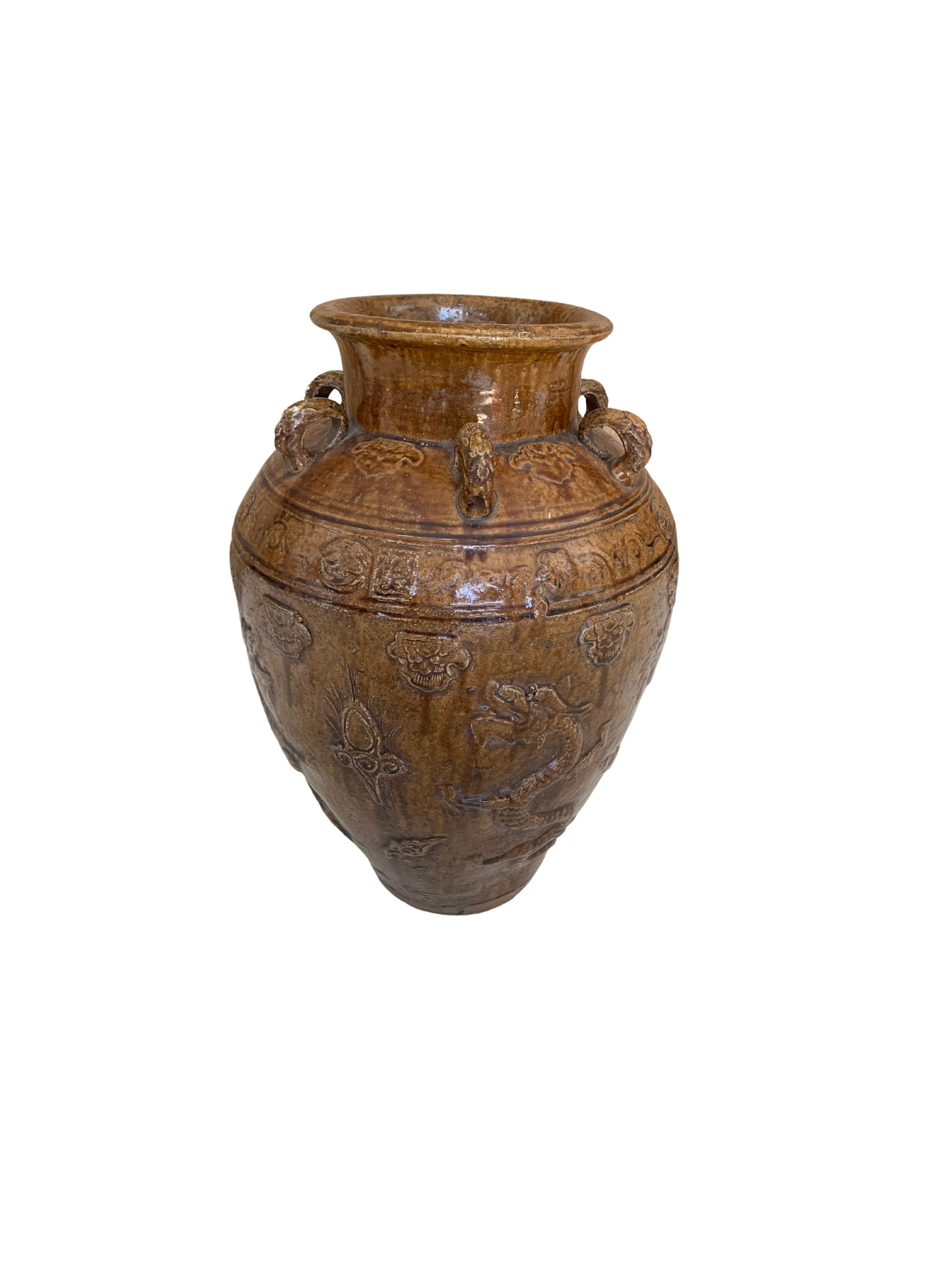This Chinese ceramic jar features a brownish / yellow glaze. In addition tiger medallions in the shape of loops wrap around the Jar’s shoulder. These were used to secure the lid to the jar and prevent the contents from leaking. Jars such as these
