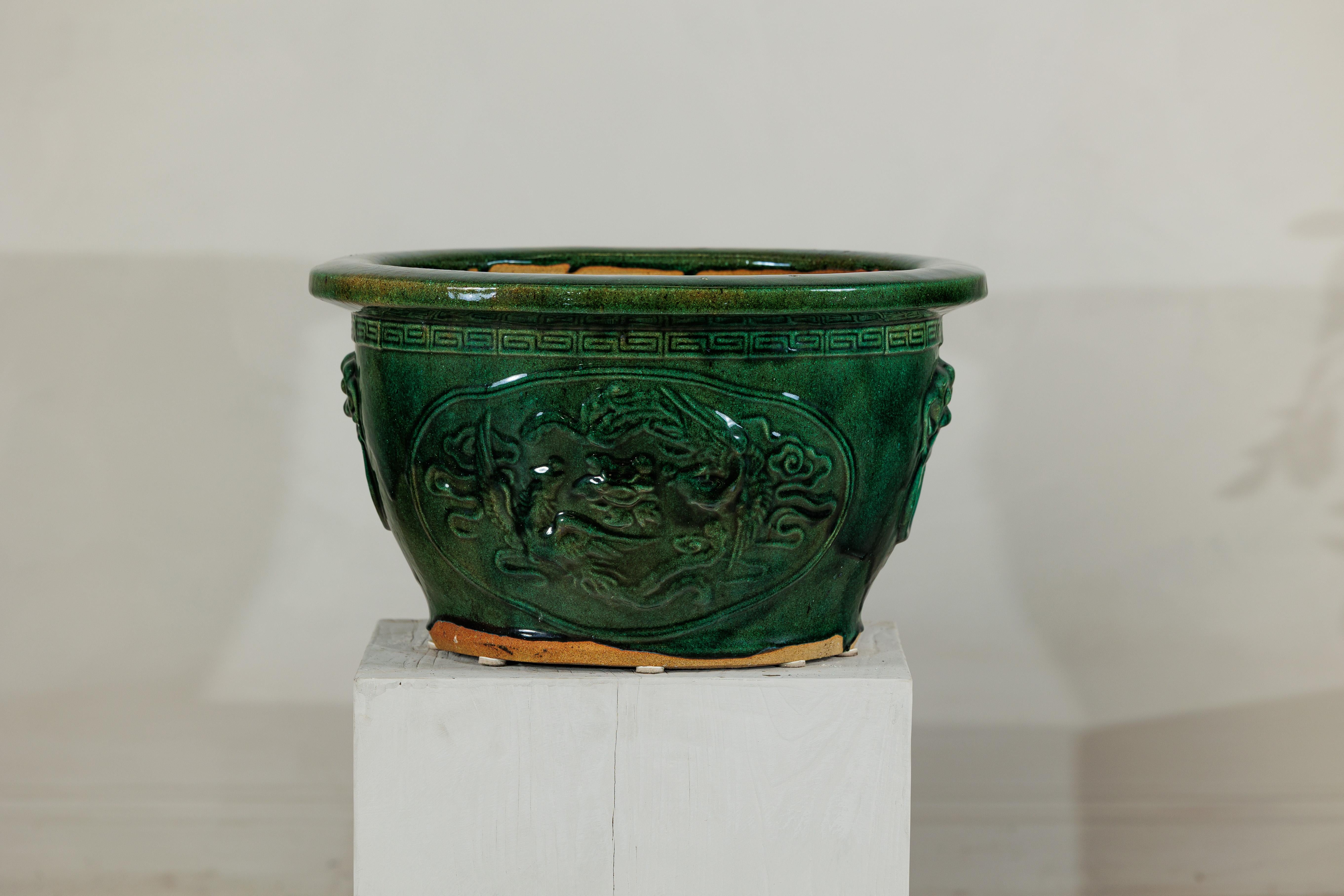Cette grande jardinière chinoise est recouverte d'une riche glaçure verte qui met en valeur son audacieux décor en relief. La forme circulaire large est définie par un épais bord roulé et des panneaux décorés représentant un dragon sinueux parmi des