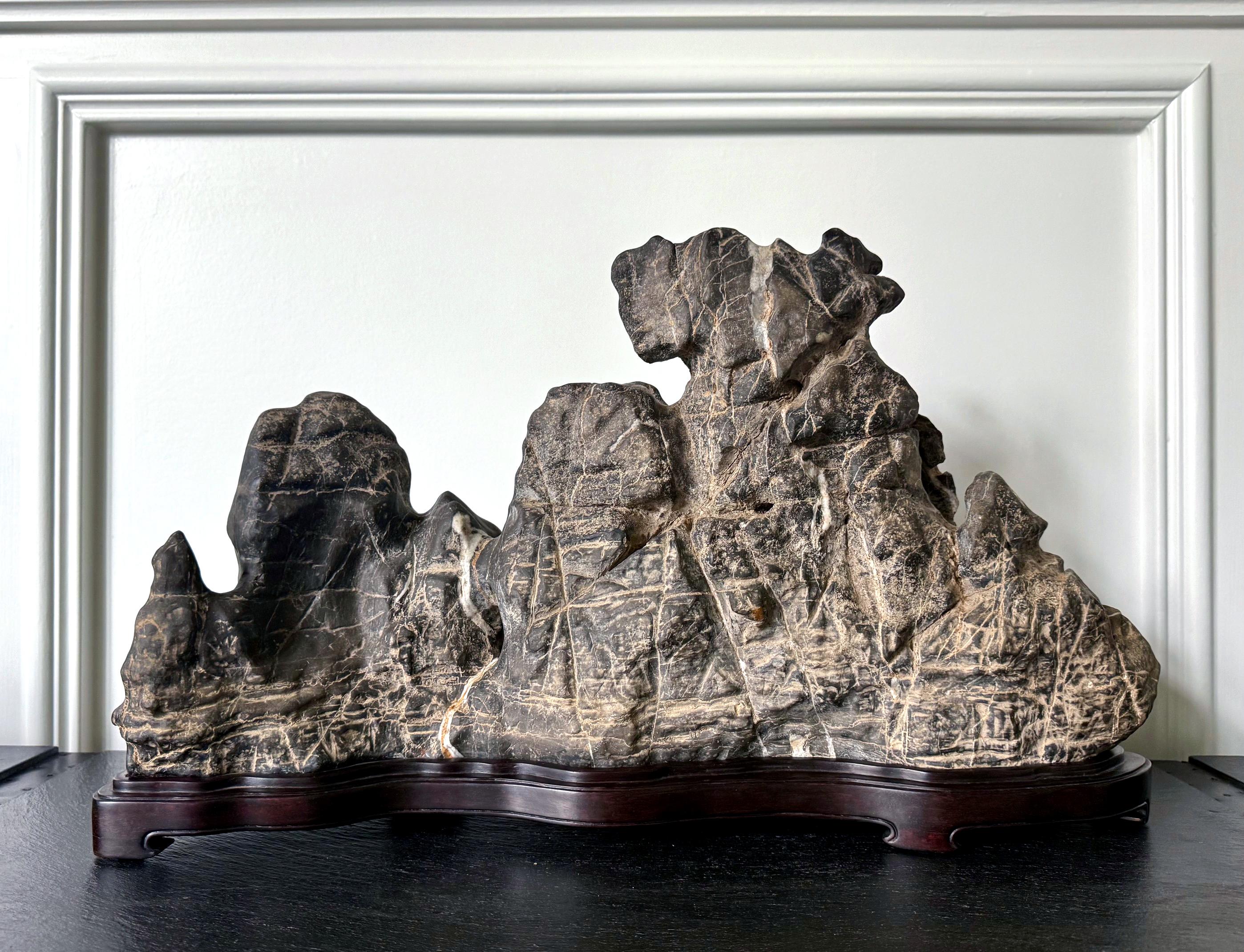 A wonderfully formed Chinese scholar stone of Lingbi type presented on a carved wood base with curvy conforming contour. Impressive in size and substantial in weight, this grey Lingbi stone manifests itself in the silouette of a horizontal mountain