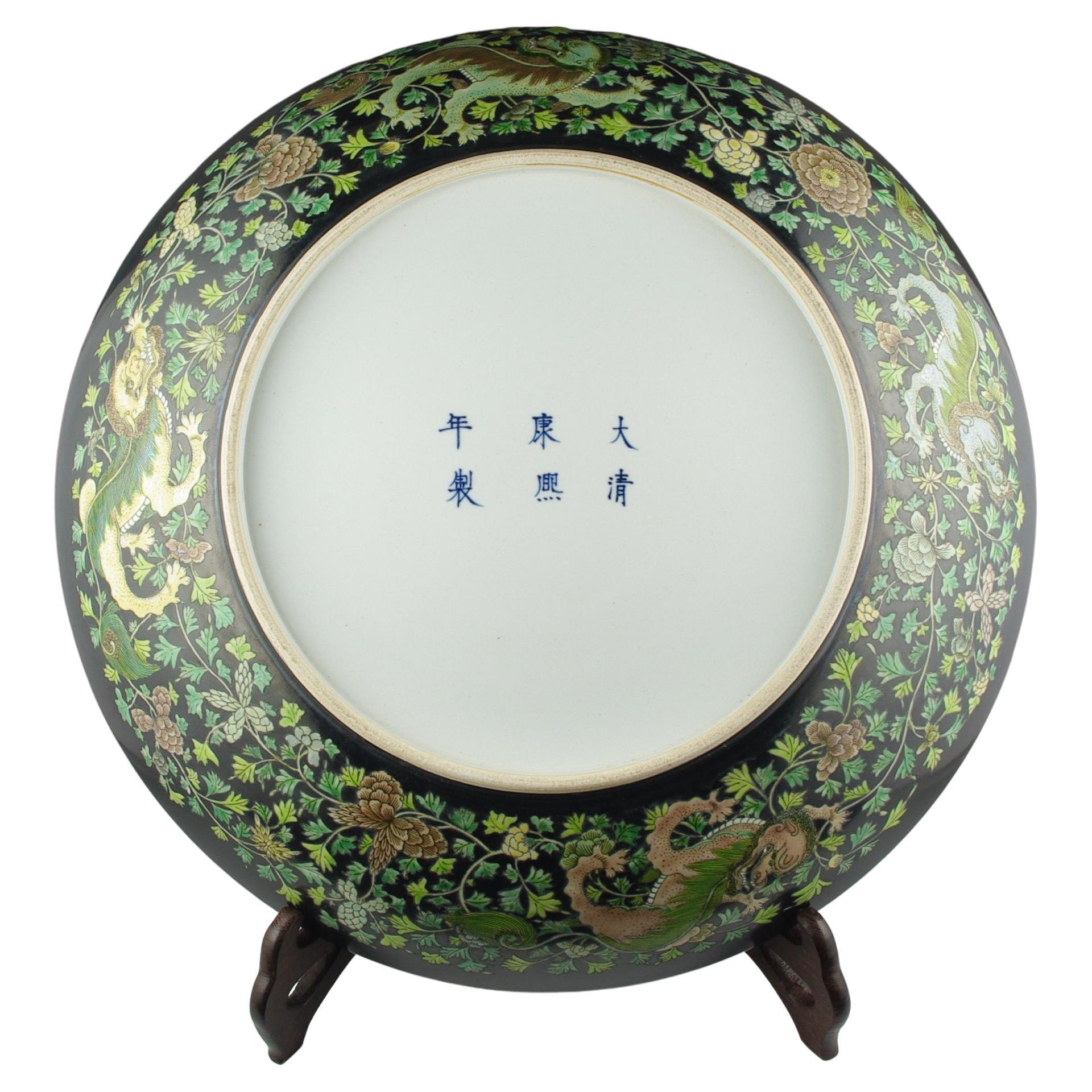 A massive Chinese famille noire porcelain charger, finely hand decorated in sancai with a center medallion and a band of foo-dogs in vines and foliage, very well executed to emulate early Qing Kangxi imperial works. This impressive charger measures