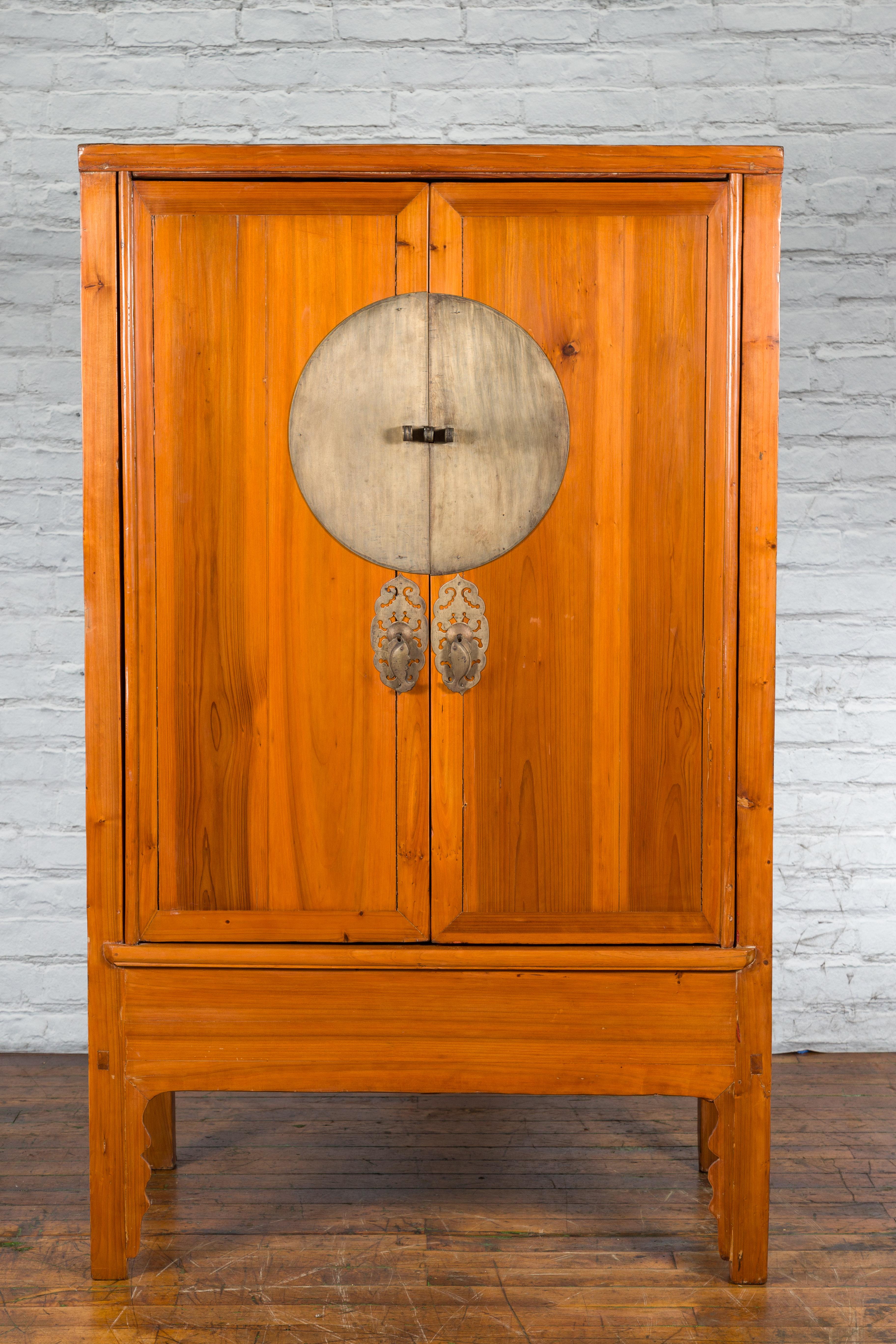 A large antique Chinese late Qing Dynasty period elmwood armoire from the early 20th century, with two doors, bronze medallion hardware, hidden drawers and carved apron. Created in China during the later years of the Qing Dynasty in the 20th
