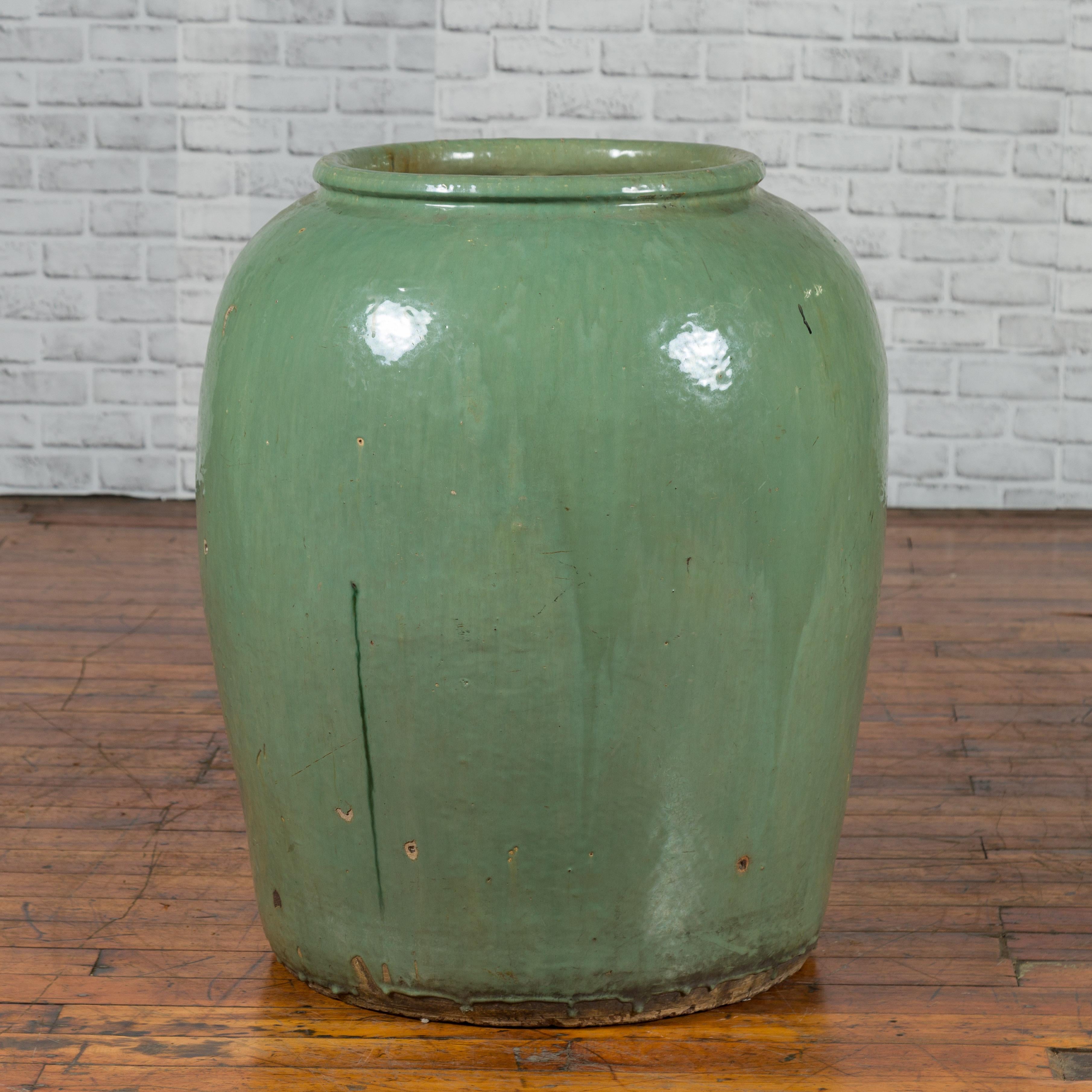 A large Chinese Qing dynasty green glazed storage jug from the 19th century with dripping touches. Created in China during the Qing dynasty period, this green jug captures our attention with its large proportions and nicely distressed patina.