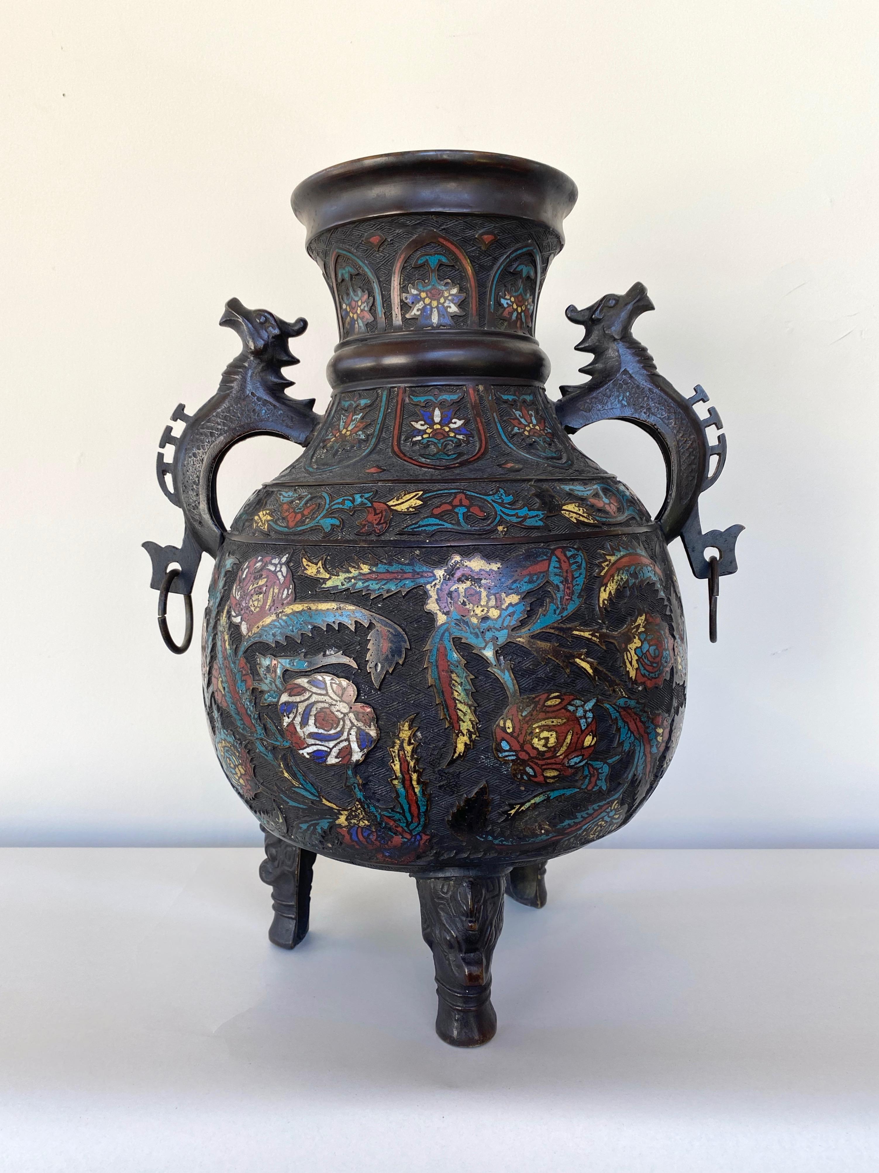 A large 19th century Chinese Qing dynasty solid bronze cloisonné urn or vessel with dragon handles and feet.

Ample form with dark patina features colorful cloisonné floral and leaf decorations in relief against an exactingly executed geometric