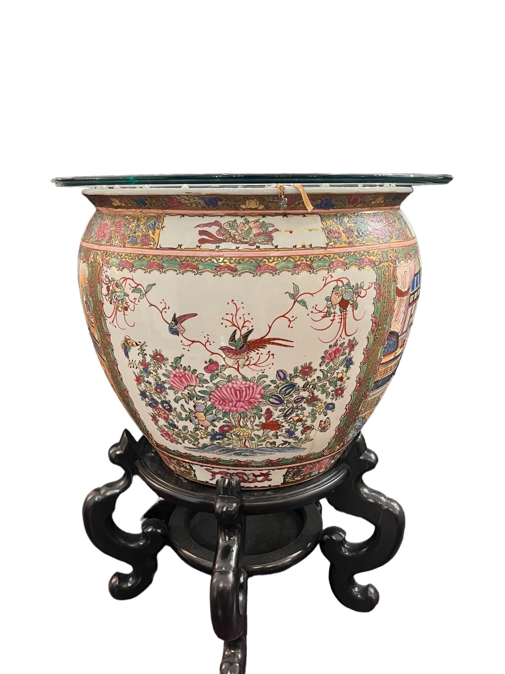This 20th-century Chinese Rose Medallion Porcelain Fish Pot possesses timeless elegance. Adorned with intricate village scenes, vibrant floral motifs, and delicate birds, it captivates with its storytelling charm. Gold gilding adds a touch of
