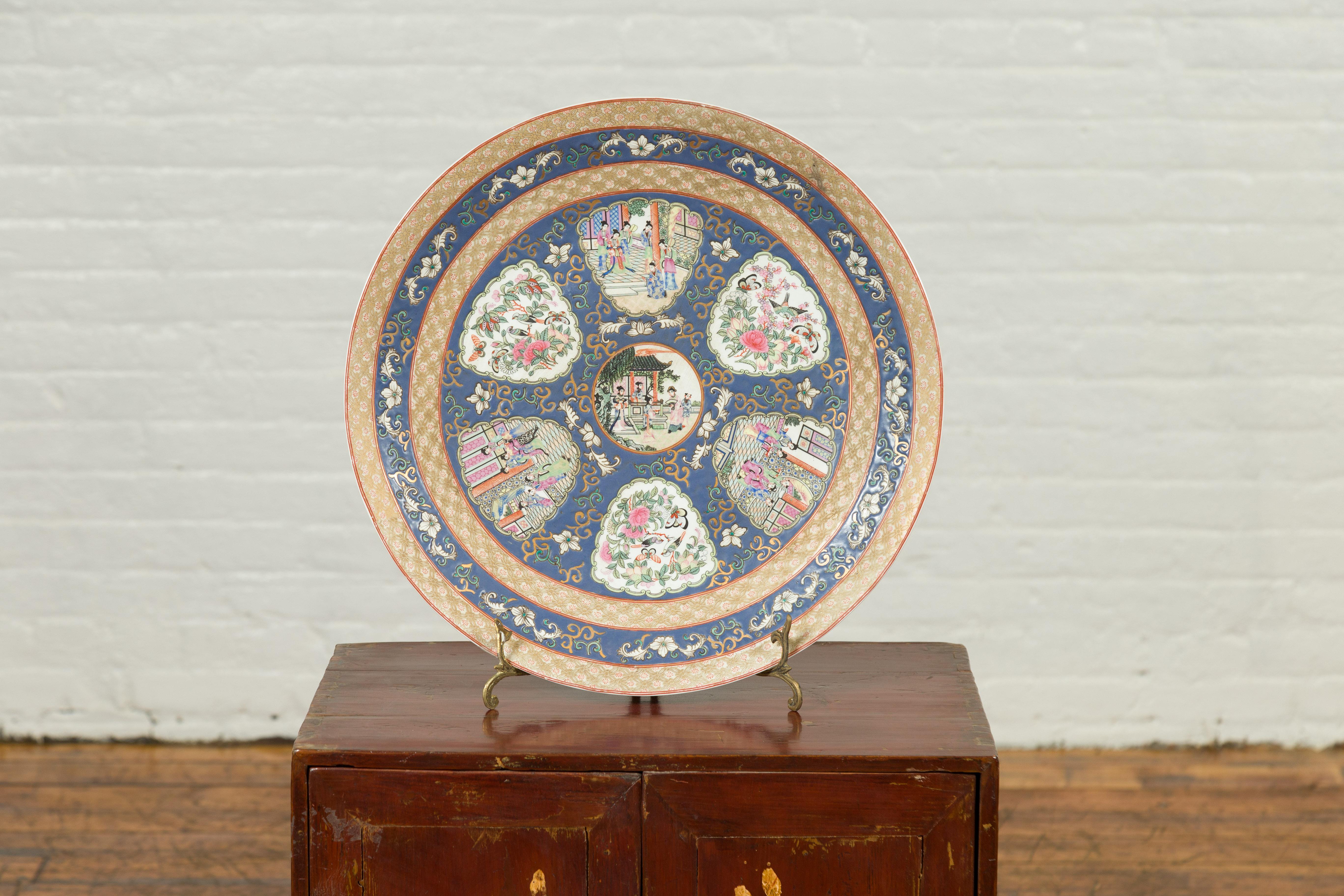 A large contemporary Chinese rose medallion hand painted porcelain platter with court scenes, flowers and butterflies. Attracting our eye with its harmoniously organized decor, this round hand painted porcelain platter, showcasing a blue ground, is