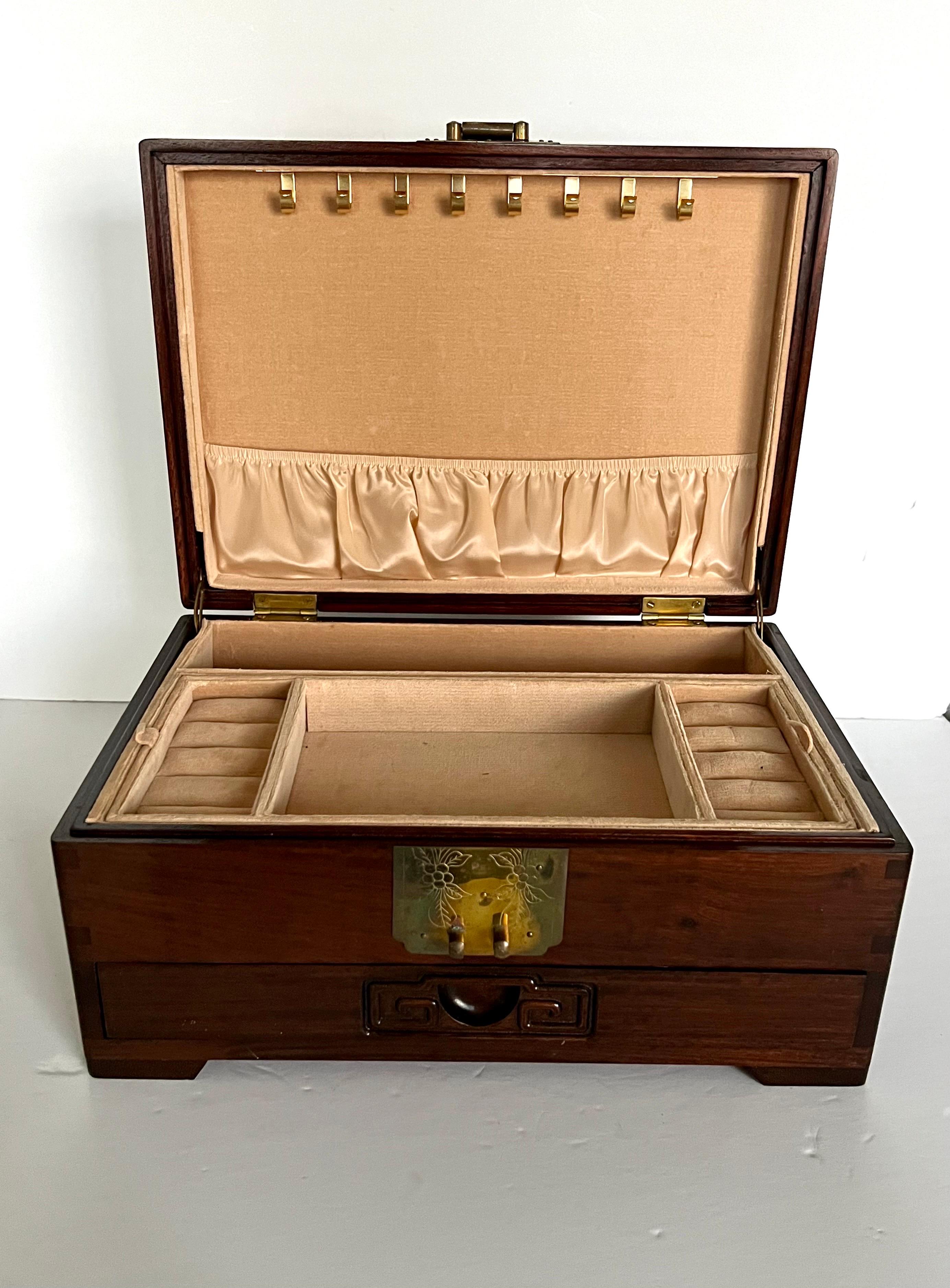 Here is nice large Chinese rosewood jewelry box with ornate solid brass fitting with a round longevity symbol carved in the middle and light peach felt lining inside. Comes with lock and key 
Has a silk interior in a beautiful peach color with a