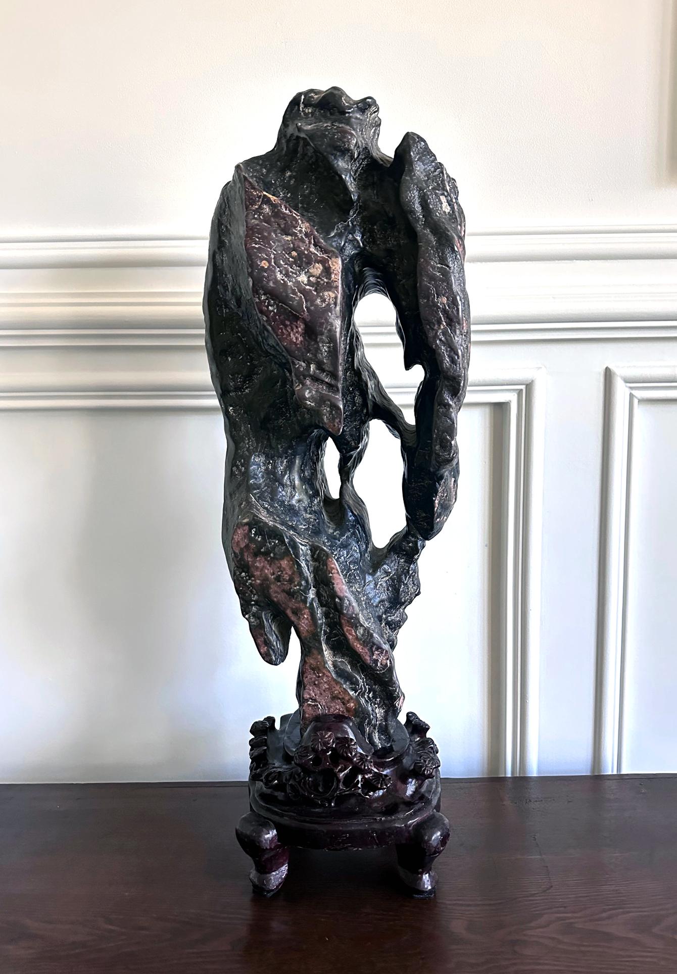 Impressionnante pierre Lingbi d'érudit chinois (également connue sous le nom de Gong Shi en chinois ; pierre de méditation et pierre spirituelle en Occident) d'une hauteur et d'une masse considérables sur un présentoir en bois sculpté. La pierre