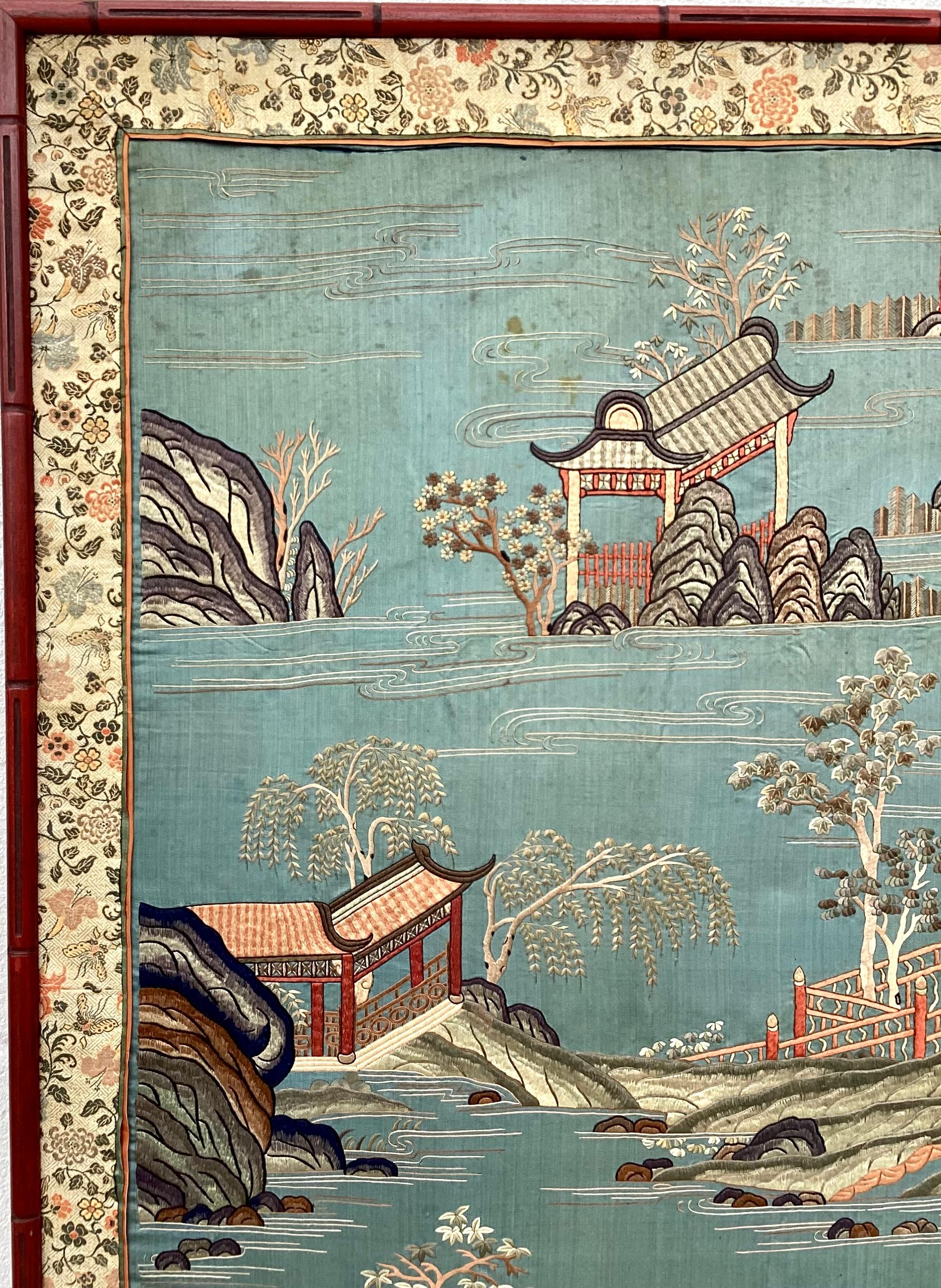This tall Chinese silk embroidery depicts Asian figures and scenes of boats, bridges and Asian landscapes. Features red, green, salmon and white colors on a beautiful serene blue background. It is framed with a red faux bamboo frame.