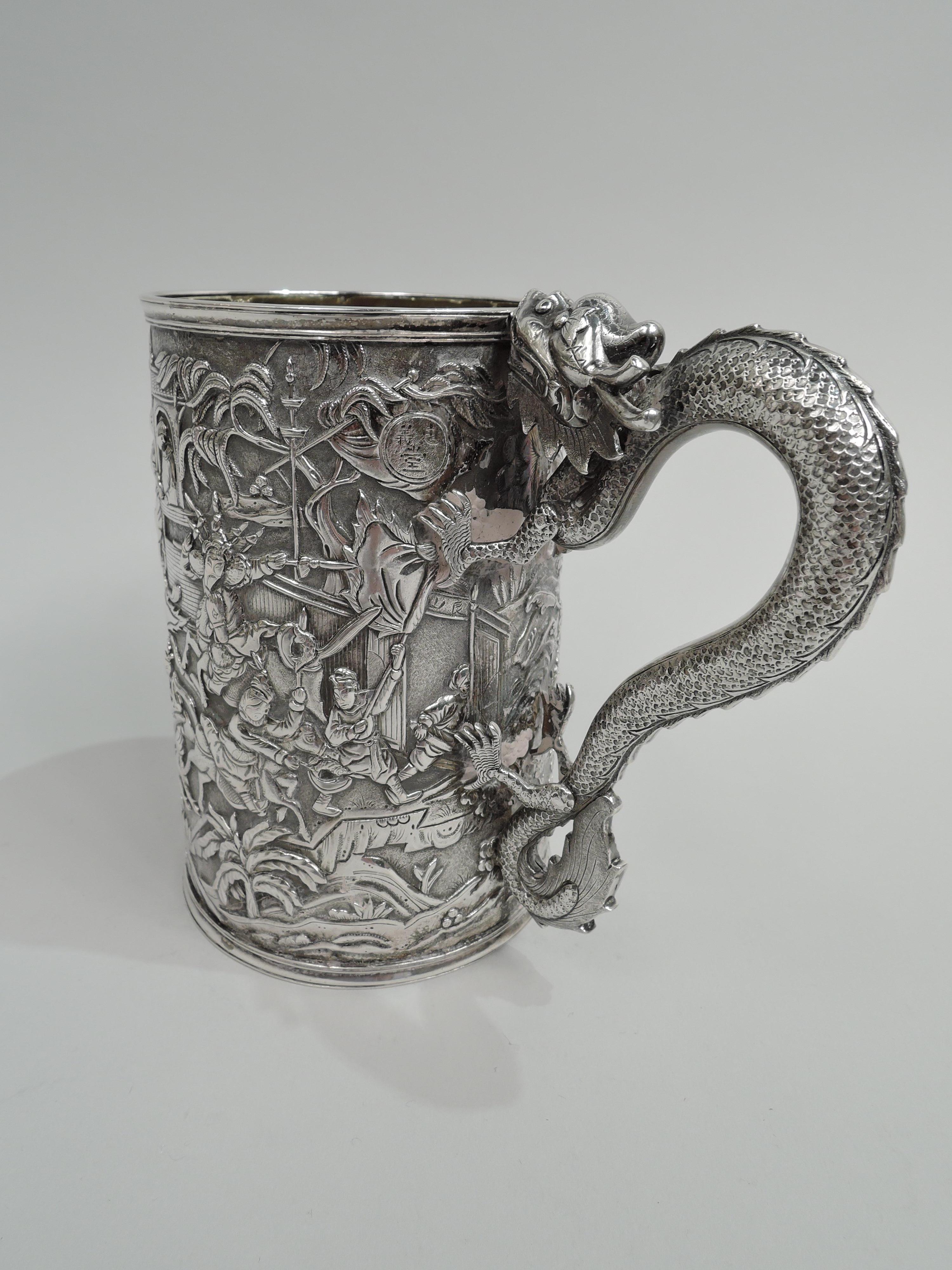 Large Chinese silver mug, late 19th century. Straight and upward tapering sides with dense low-relief frieze on stippled ground: A battle with spearmen, flag bearers, swordsmen, and lancers. An open gate indicates the direction of the fighting.
