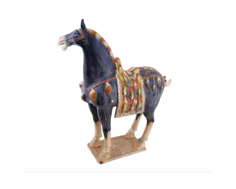 A large Chinese Tang Dynasty manner hand painted enamelled pottery figure of a horse. The horse is adorned with a glazed saddle with relief tassels along its body. The figure is adorned with relief elements, and foliage and traditional Greek motifs.